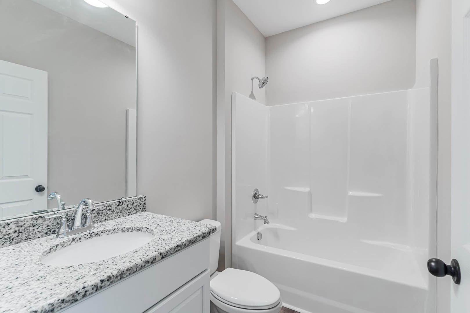 White bathroom with rectangular sink, chrome faucet, closed toilet, white bathtub, tiled walls, and black round door knob on white door