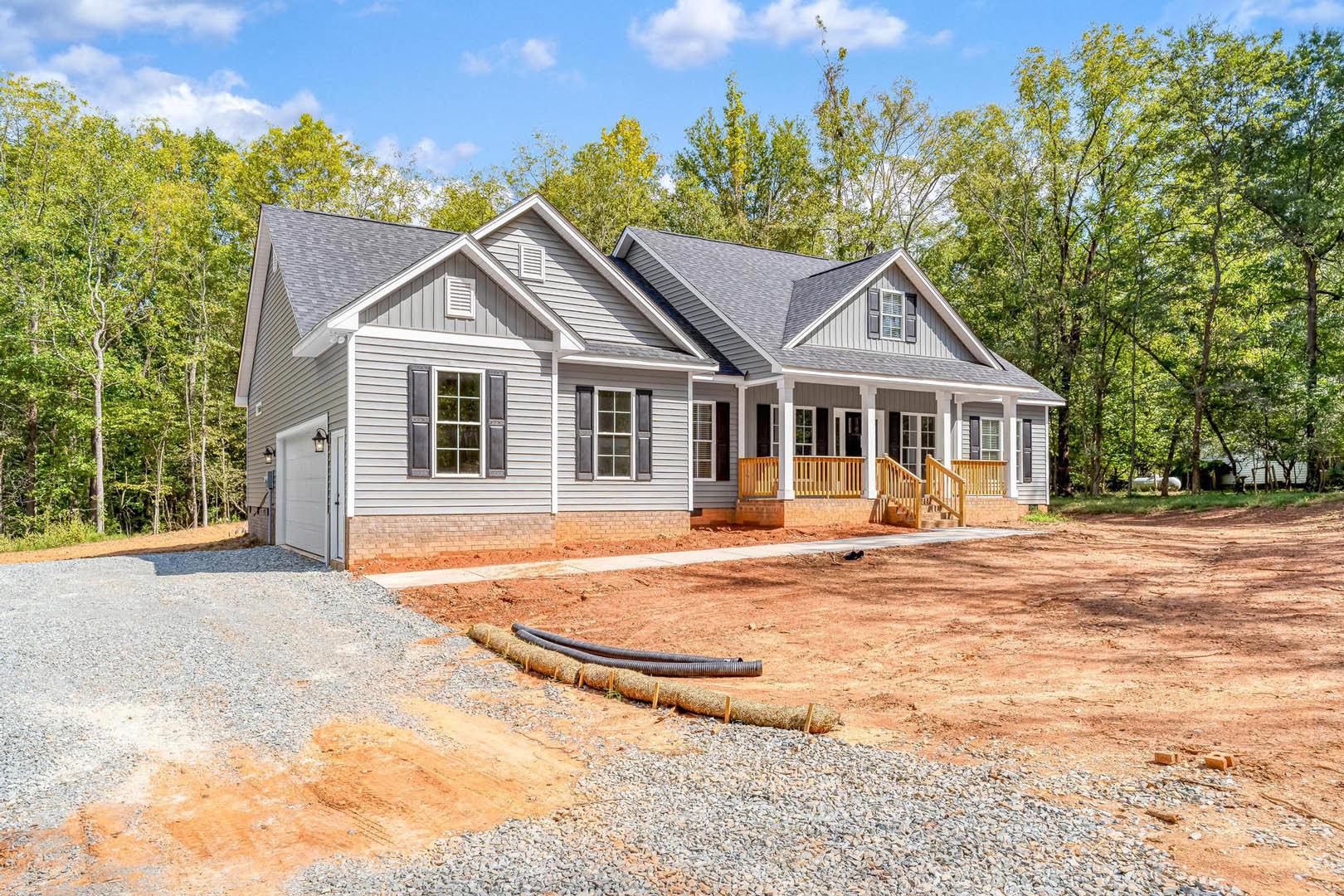 Two-story home with white siding, black shuttered windows, covered front porch, concrete driveway, and mature trees in the background