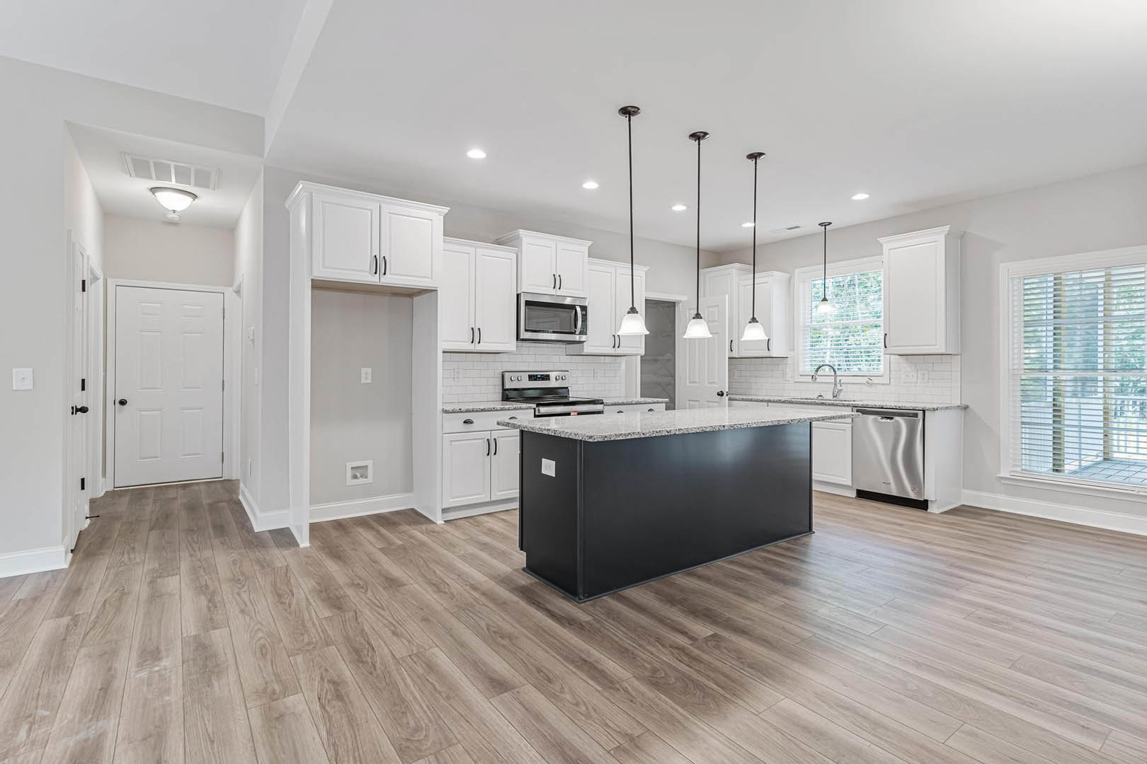 Open kitchen with wood laminate flooring, central island featuring black base and white countertop, built-in microwave, white cabinetry, stainless steel sink, white door with black