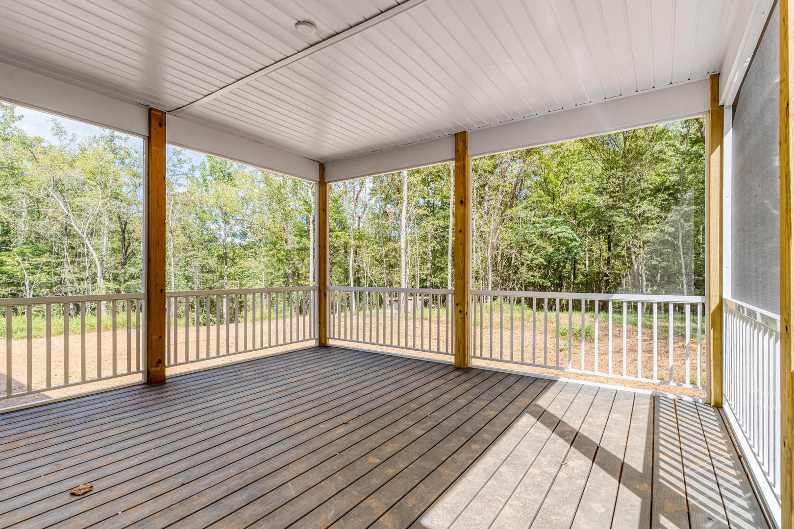 Wooden deck with white railing, white paneled ceiling, surrounded by trees, outdoor space with shaded seating area.