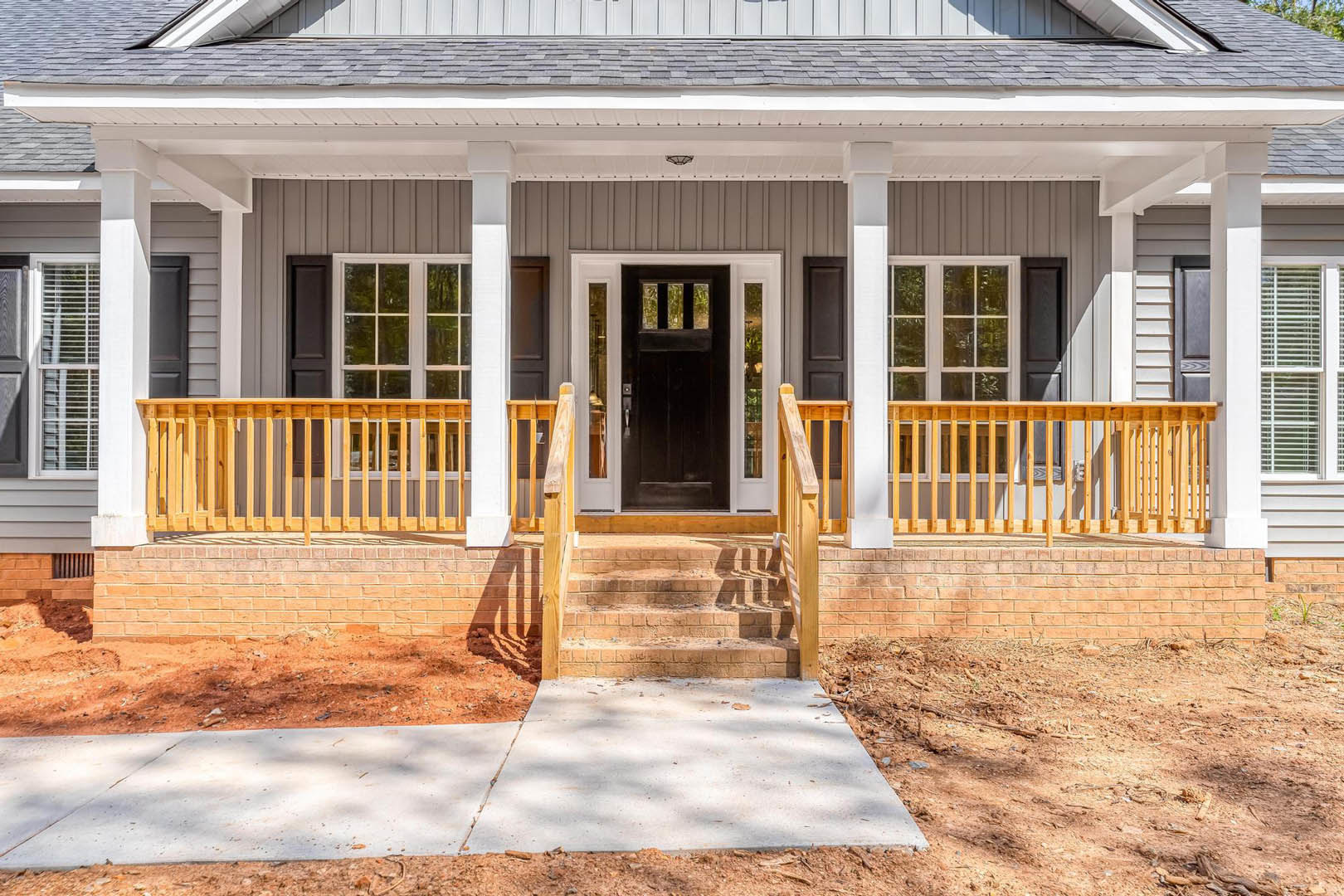 Wide front porch with white siding, dark wood door, concrete walkway showing a visible crack, steps leading up, windows flanking entry, gabled roof overhead
