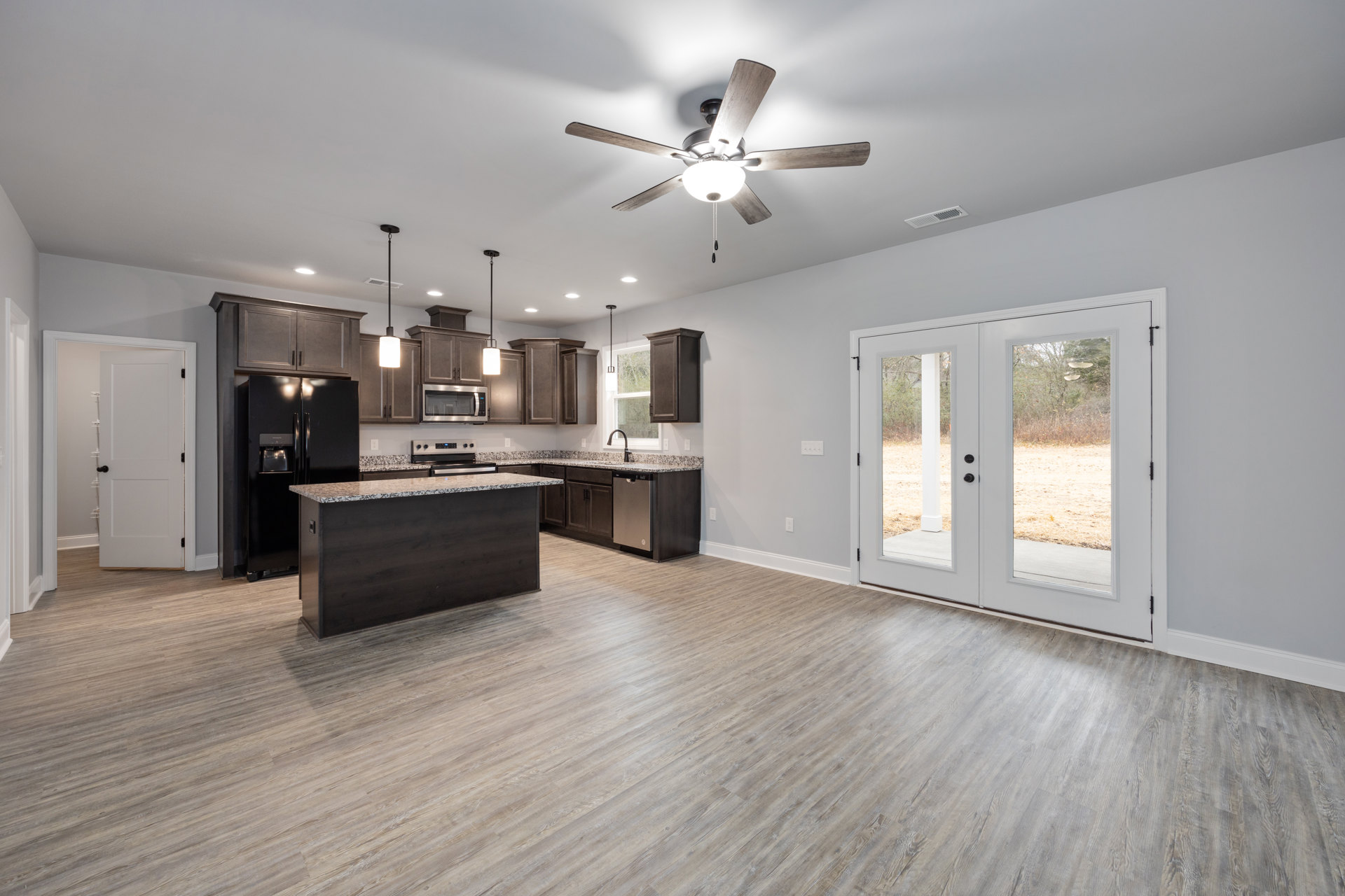 Open kitchen and dining area featuring wood flooring, black countertop, white cabinetry, built-in microwave, ceiling fan with light fixture, and double doors overlooking a green