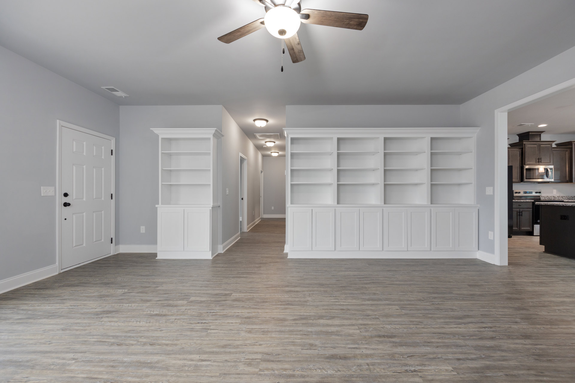 Wood floor room with white walls, built-in white shelves with cabinet doors, ceiling fan with light fixture, and white door featuring black knobs