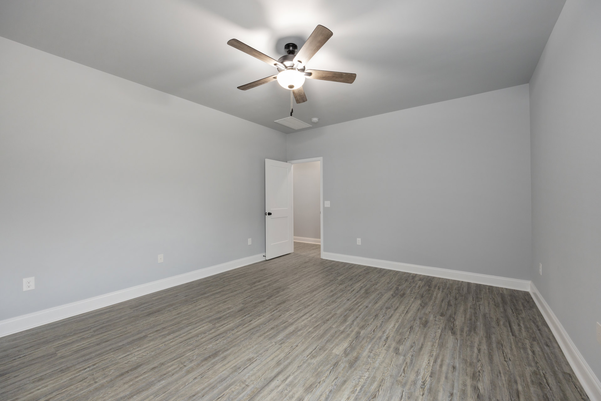 Ceiling fan with light fixture mounted on white plaster ceiling, open white door with black hardware, wood laminate flooring