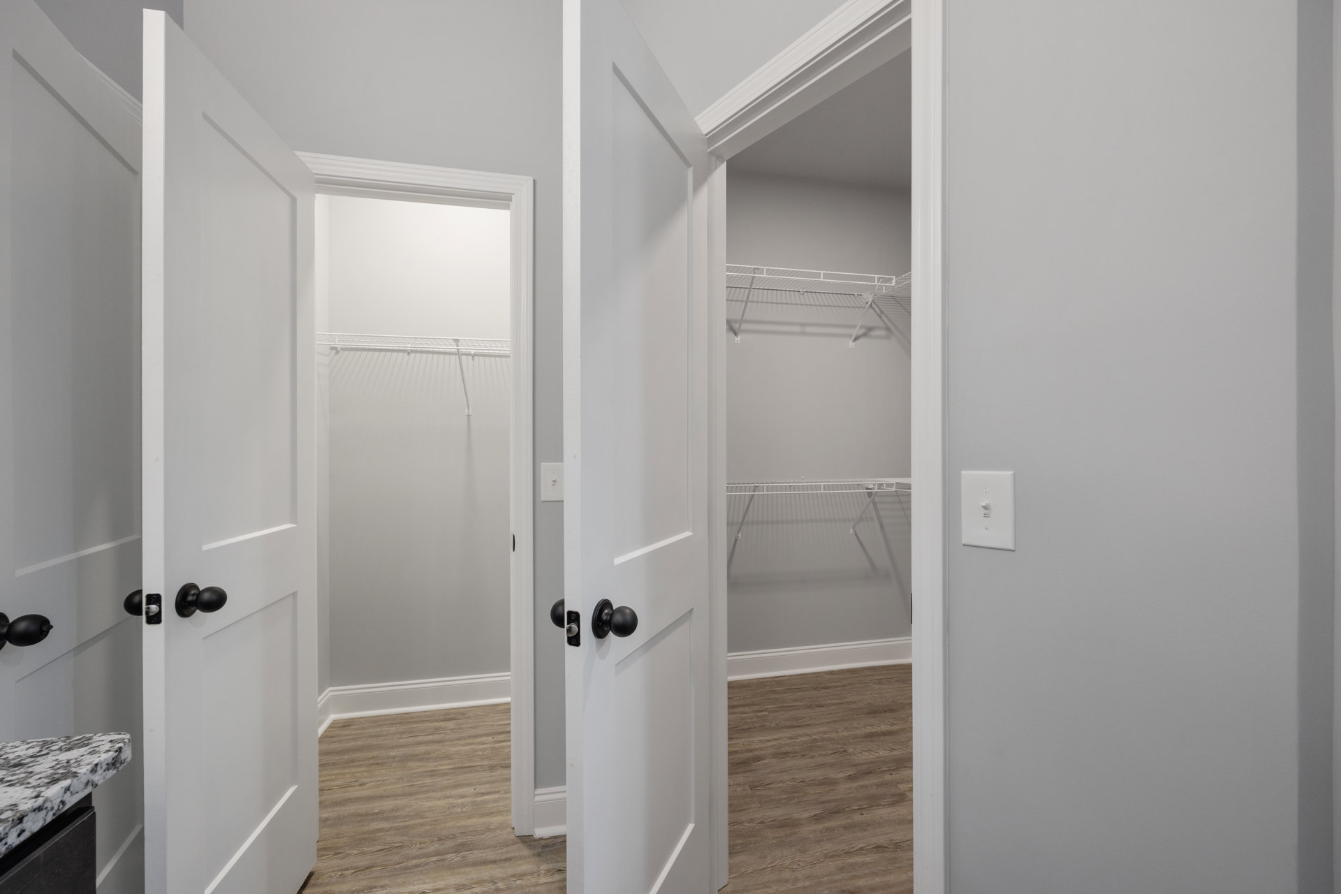 Wood floor with white baseboards, open white doors, black and white marble countertop, white wall shelf, light switch, close-up of silver door knob, bathroom tile and plumbing