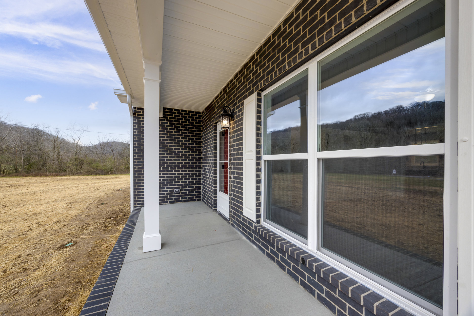 Red brick house with covered front porch, white-trimmed window, grassy yard, and cloudy sky in background