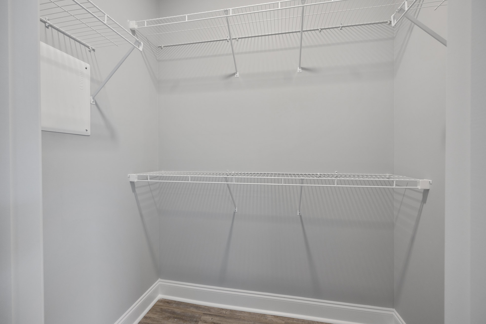 White closet with built-in shelves, wood plank flooring, and white baseboards along smooth plaster walls