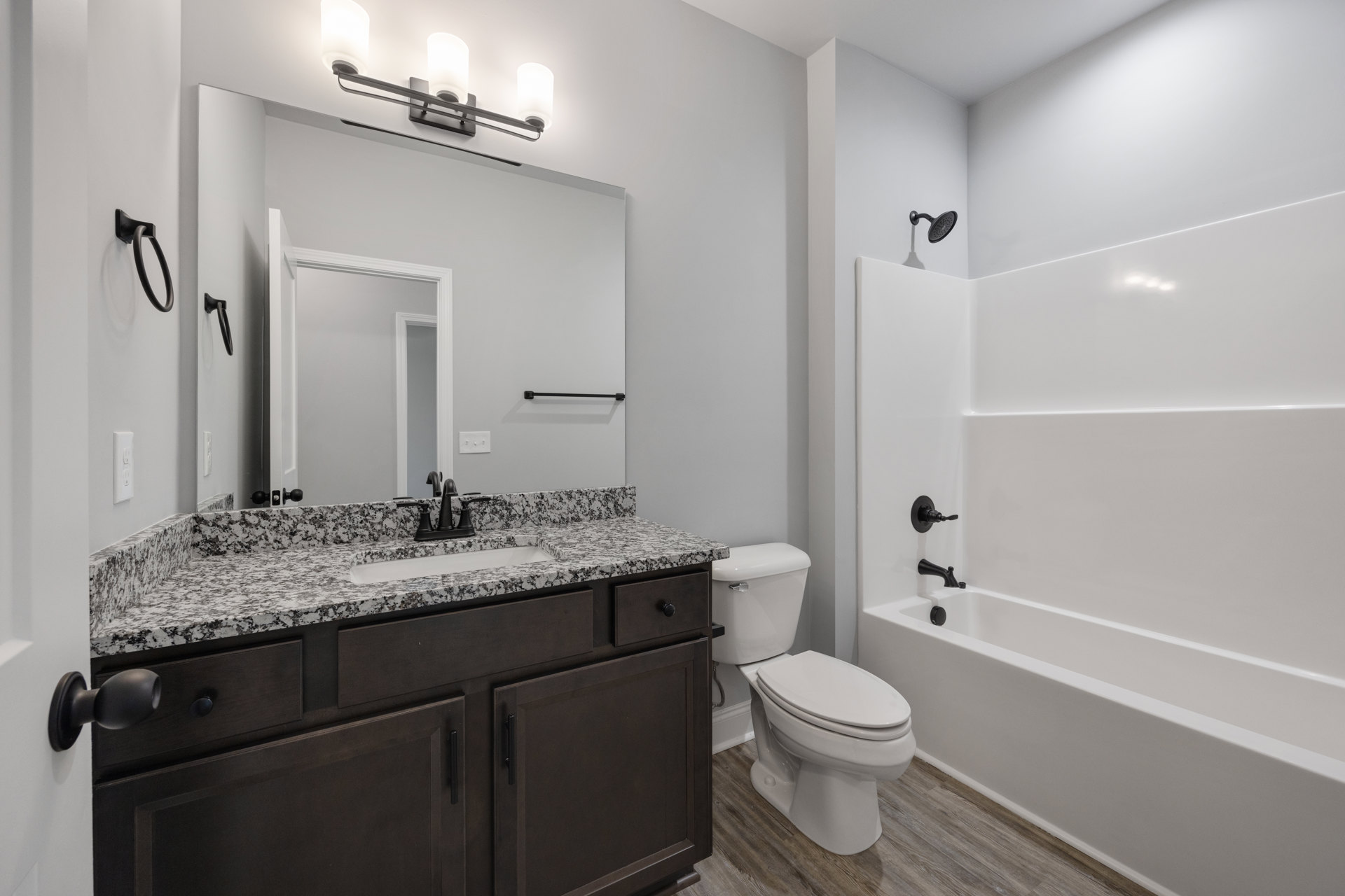 Bathroom with marble countertop, white bathtub with wall-mounted shower head, white toilet, tile flooring, and a black cable plugged into the wall