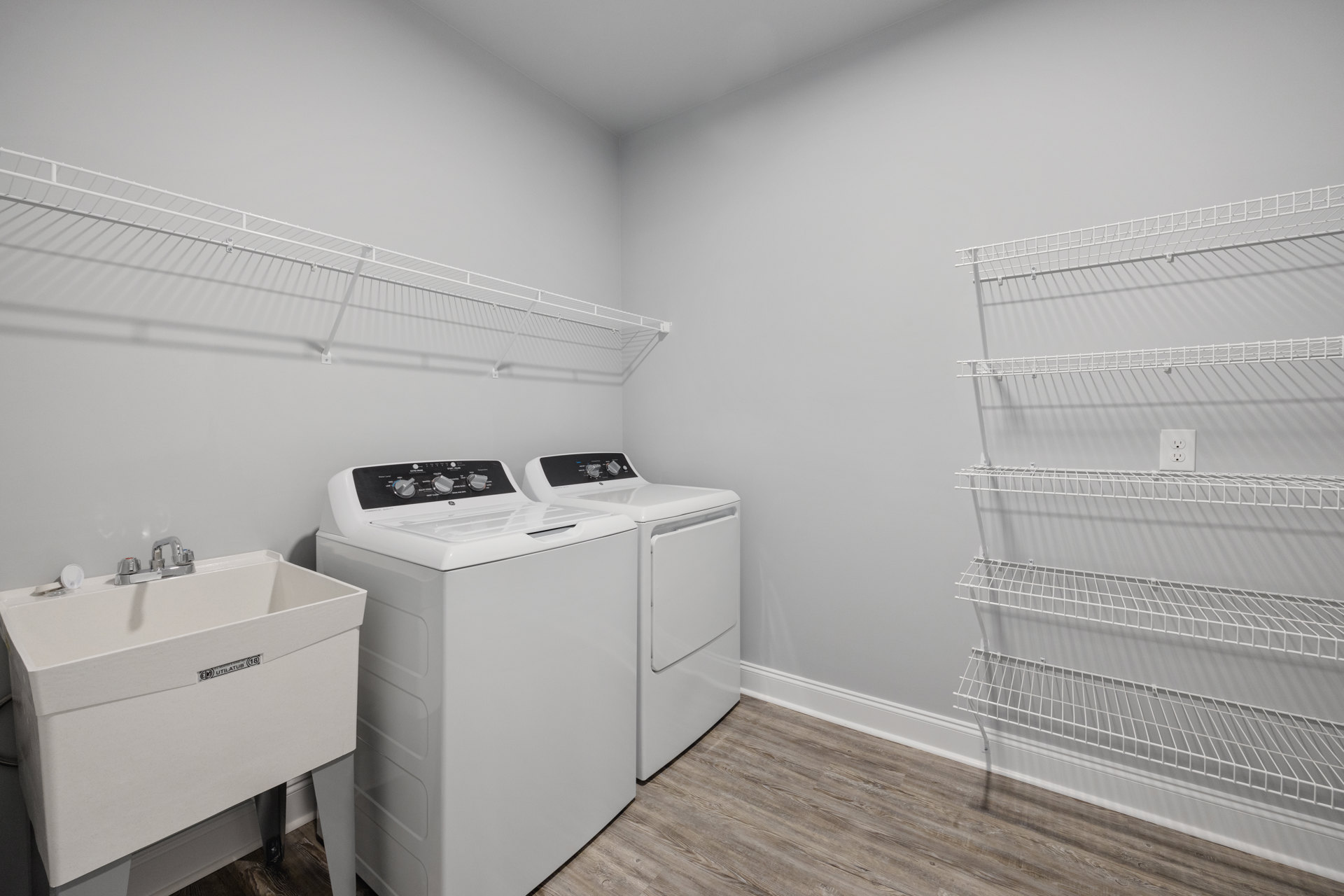 Laundry room with white washing machine, white sink, wire shelving on wall, cabinetry, and light-colored flooring