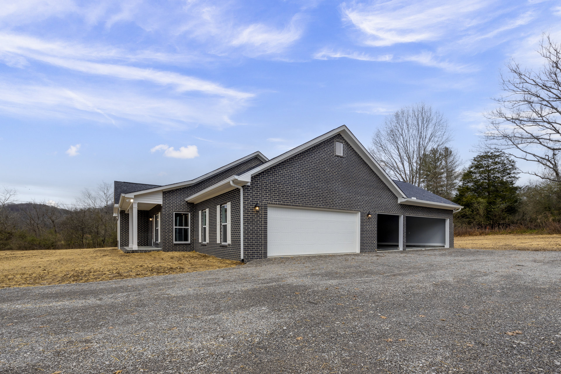 Red brick house with attached garage, white-framed windows, and garage door, set against blue sky with trees and landscaping