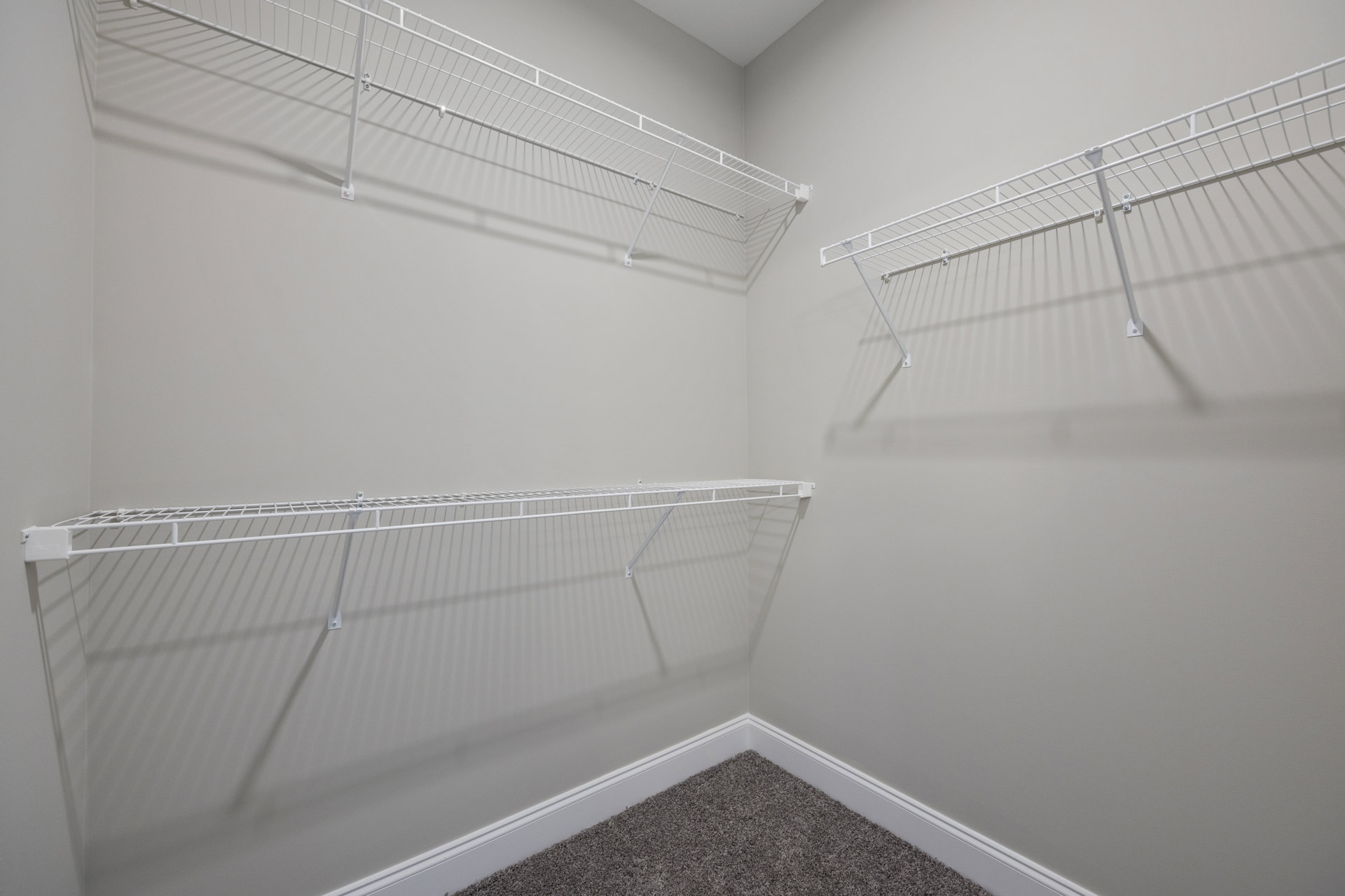 White built-in shelves mounted on a plaster wall above a light carpeted floor, with a white metal rod secured by metal bolts.