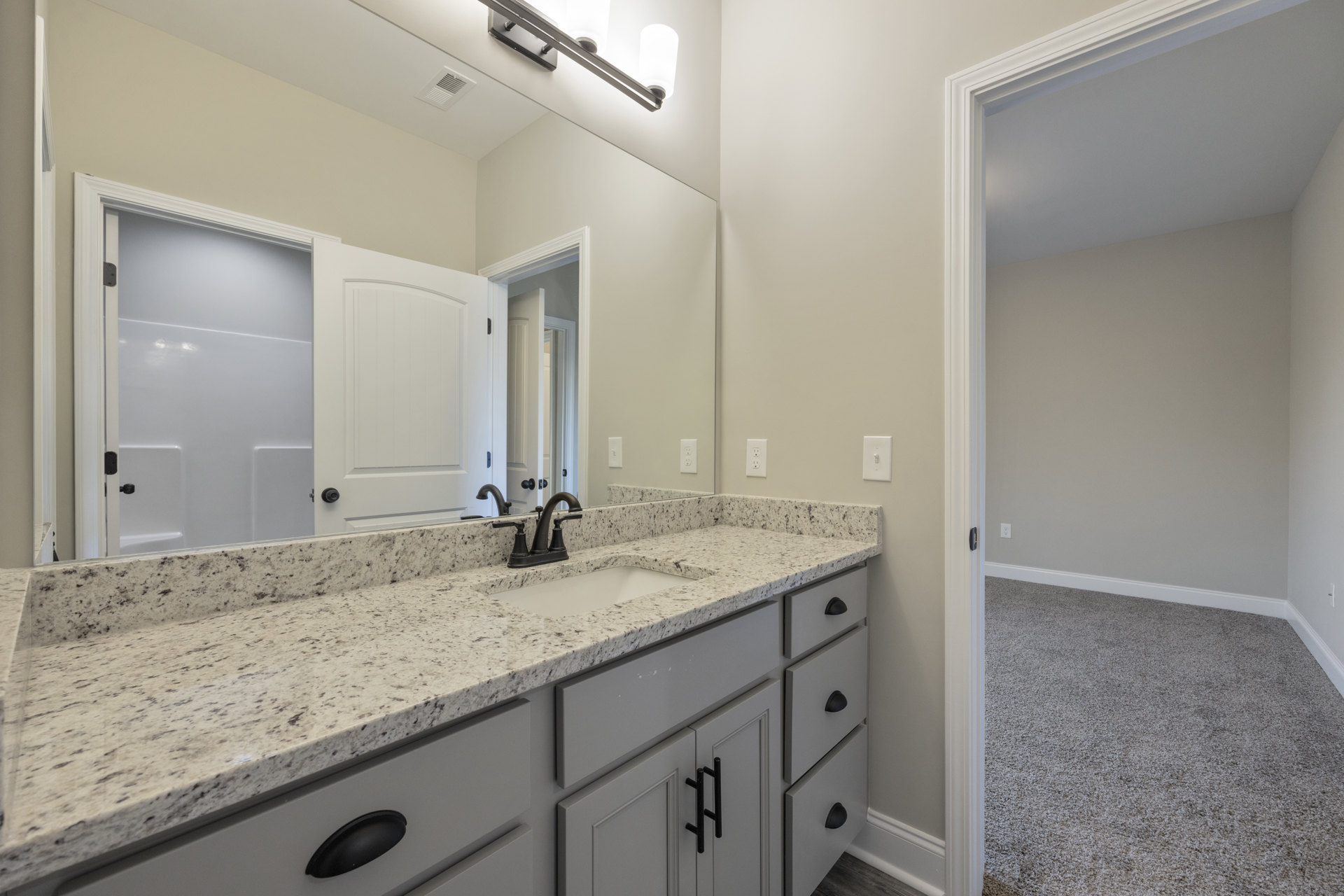 Marble countertop with undermount sink, white cabinetry, black oval soap dish, white paneled door, light tile flooring