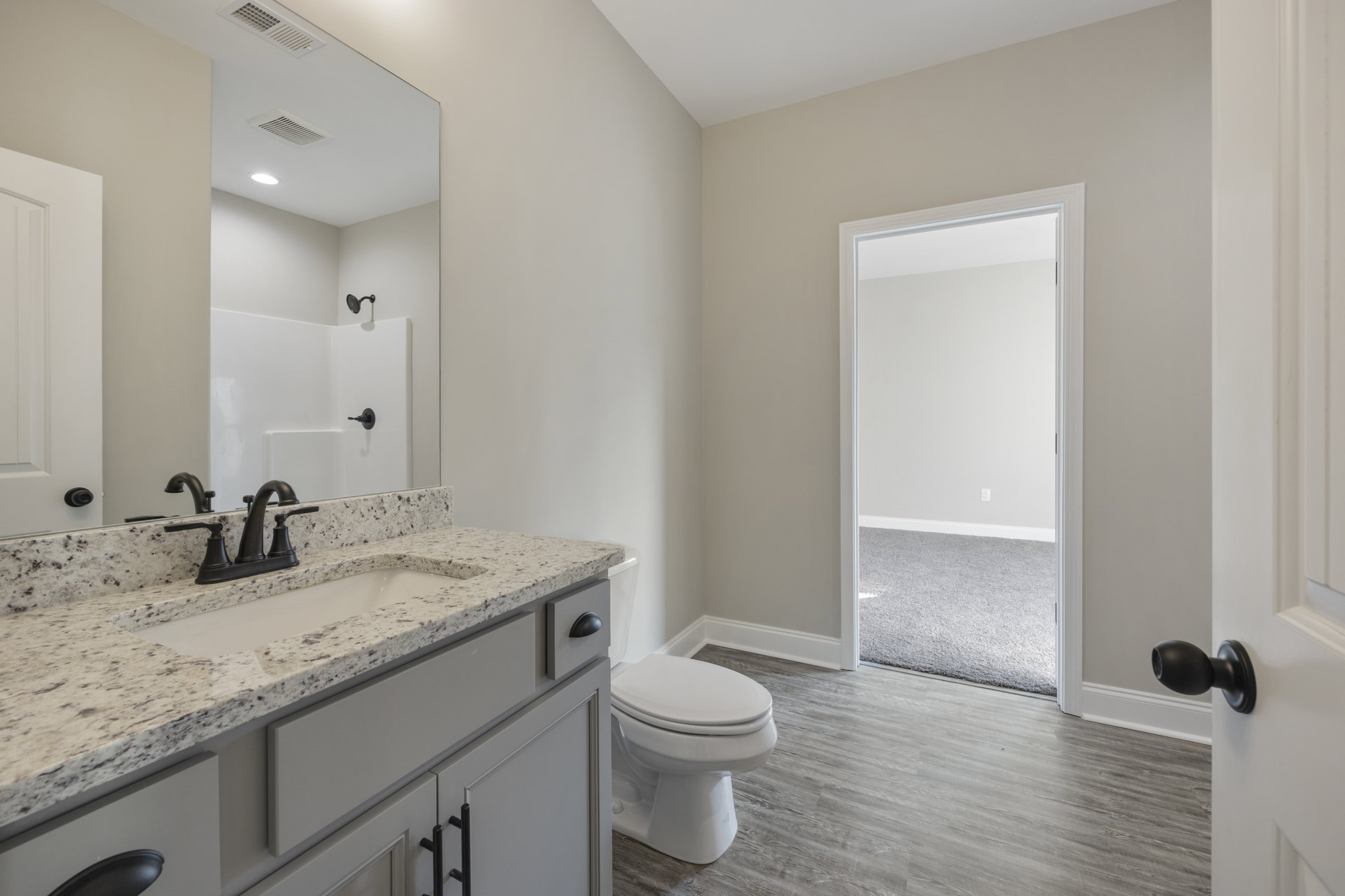 Bathroom with white toilet, marble countertop sink, dark cabinetry, and black metal soap dispenser on counter; white door frame and tiled floor visible.