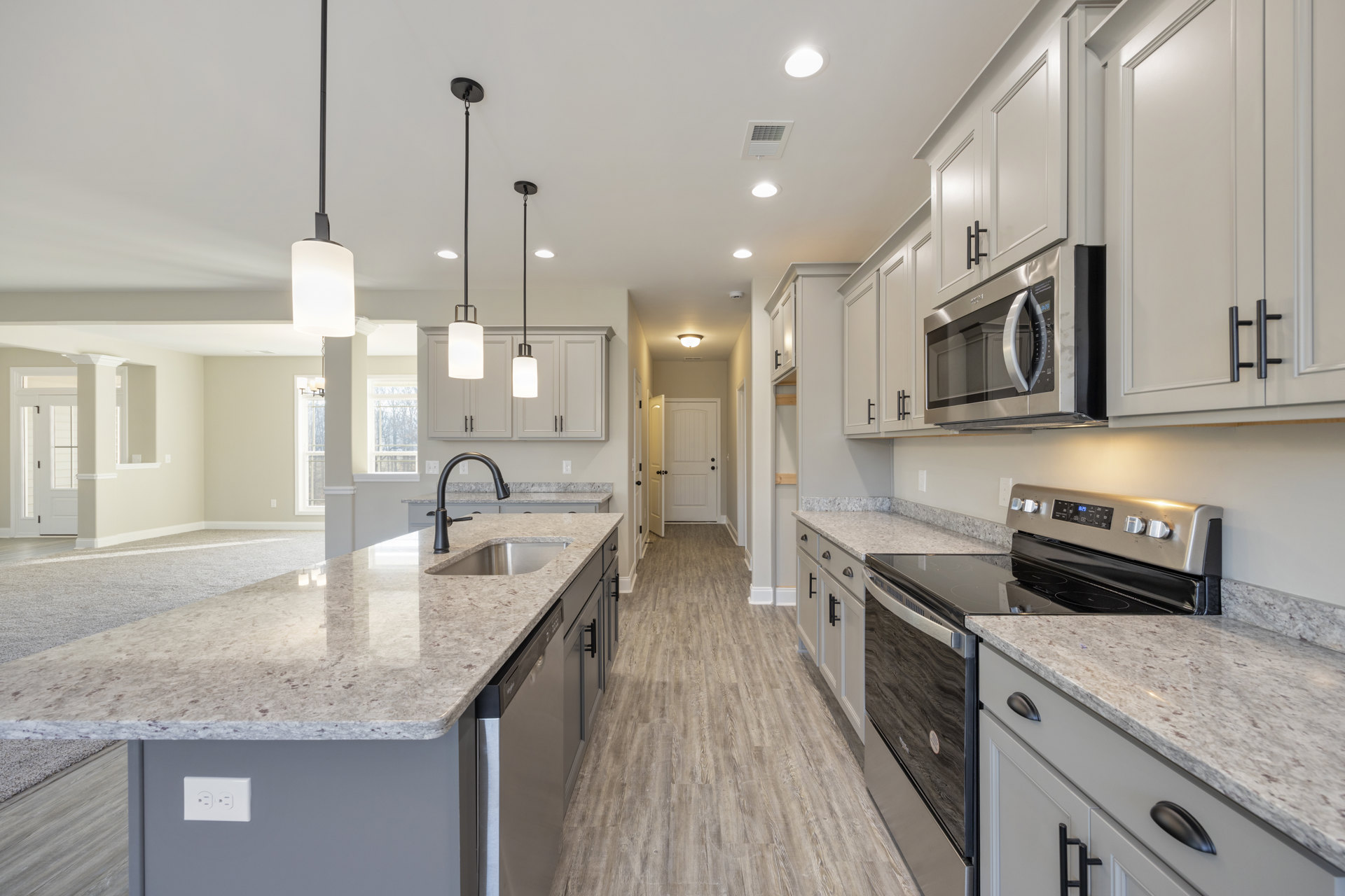 Granite countertops, stainless steel stove, kitchen island with sink and faucet, white cabinetry, ceiling light, microwave oven, vent, white door with black knobs, tiled backsplash