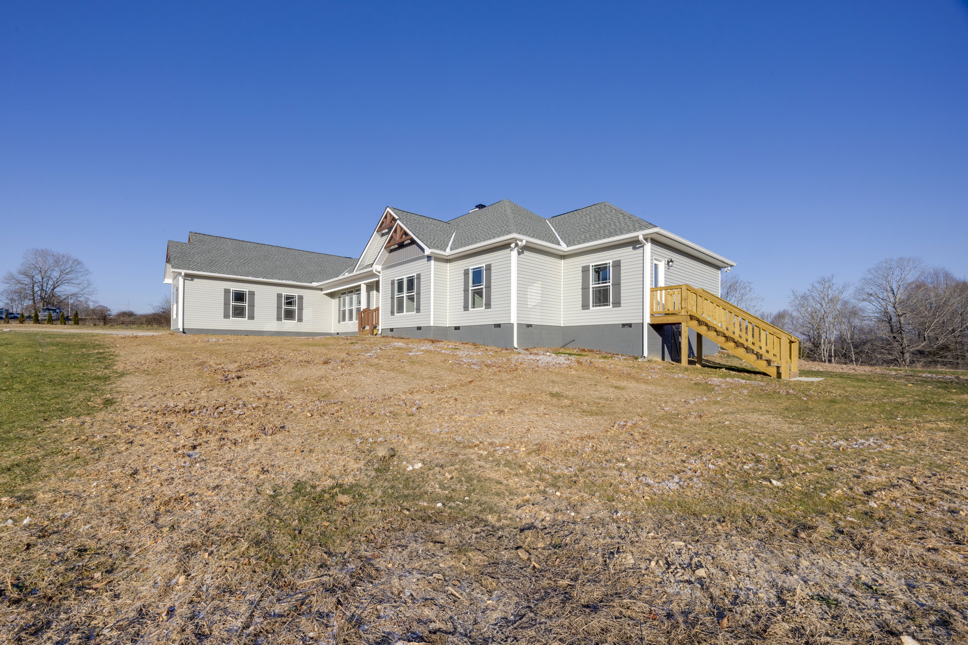 Two-story farmhouse with white siding, large windows, covered porch, wooden staircase leading to front entrance, surrounded by grass and trees.