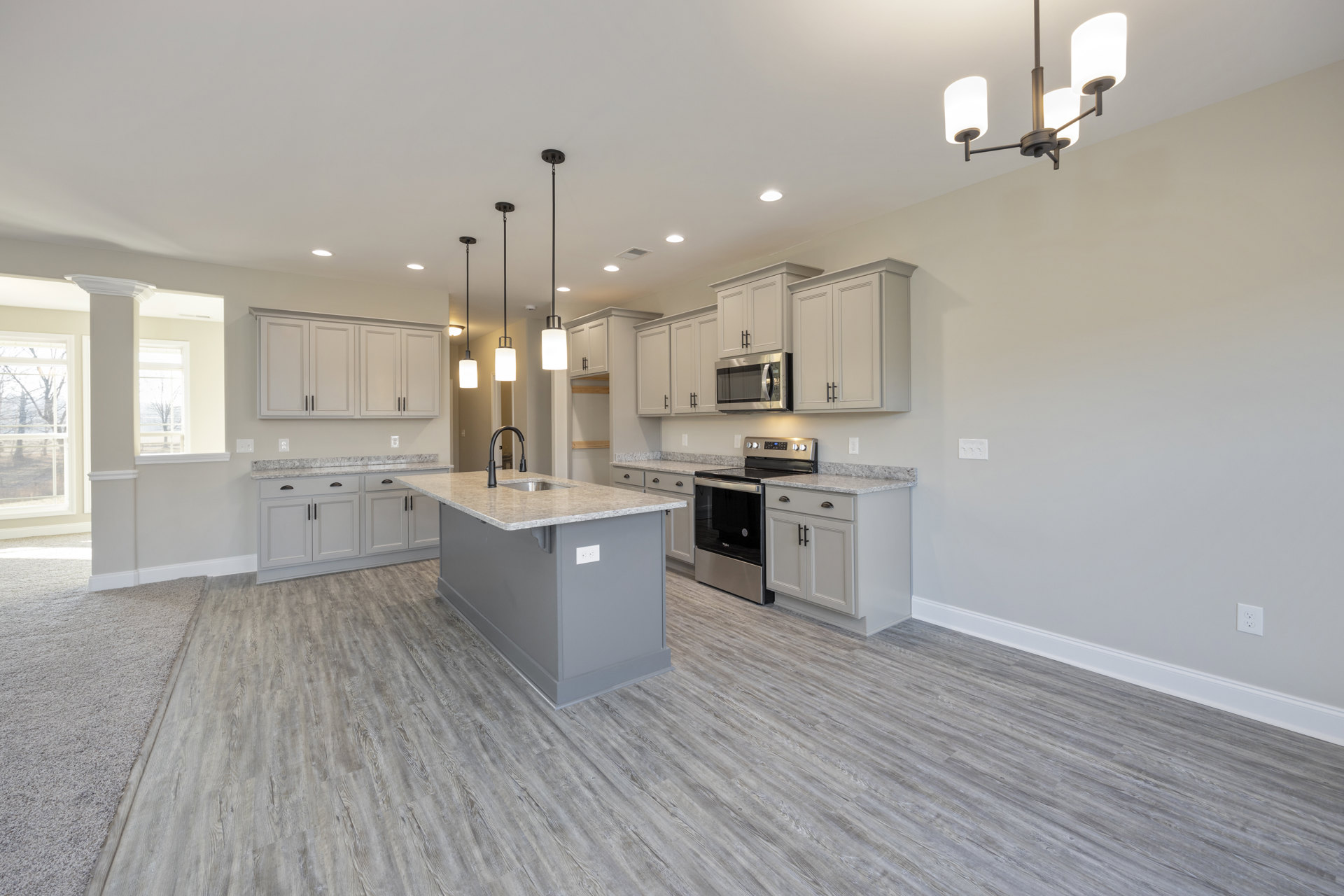 Spacious kitchen featuring a large island with a built-in sink and black faucet, white countertops, tile backsplash, stainless steel stove and oven, microwave with door, and light