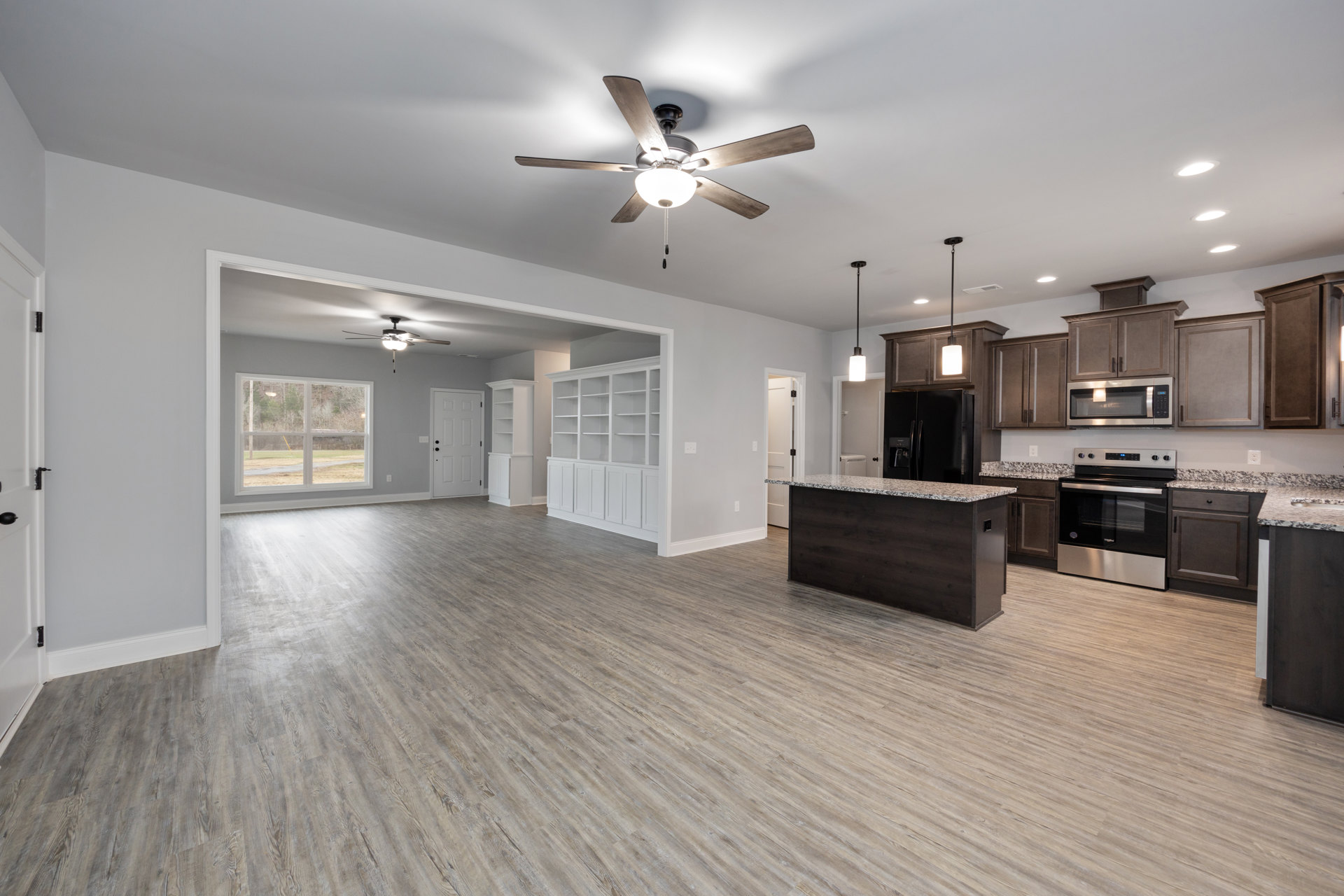 Open floor plan featuring hardwood flooring, marble kitchen island, white cabinetry, stainless steel appliances including microwave and glass-door stove, ceiling fan with light