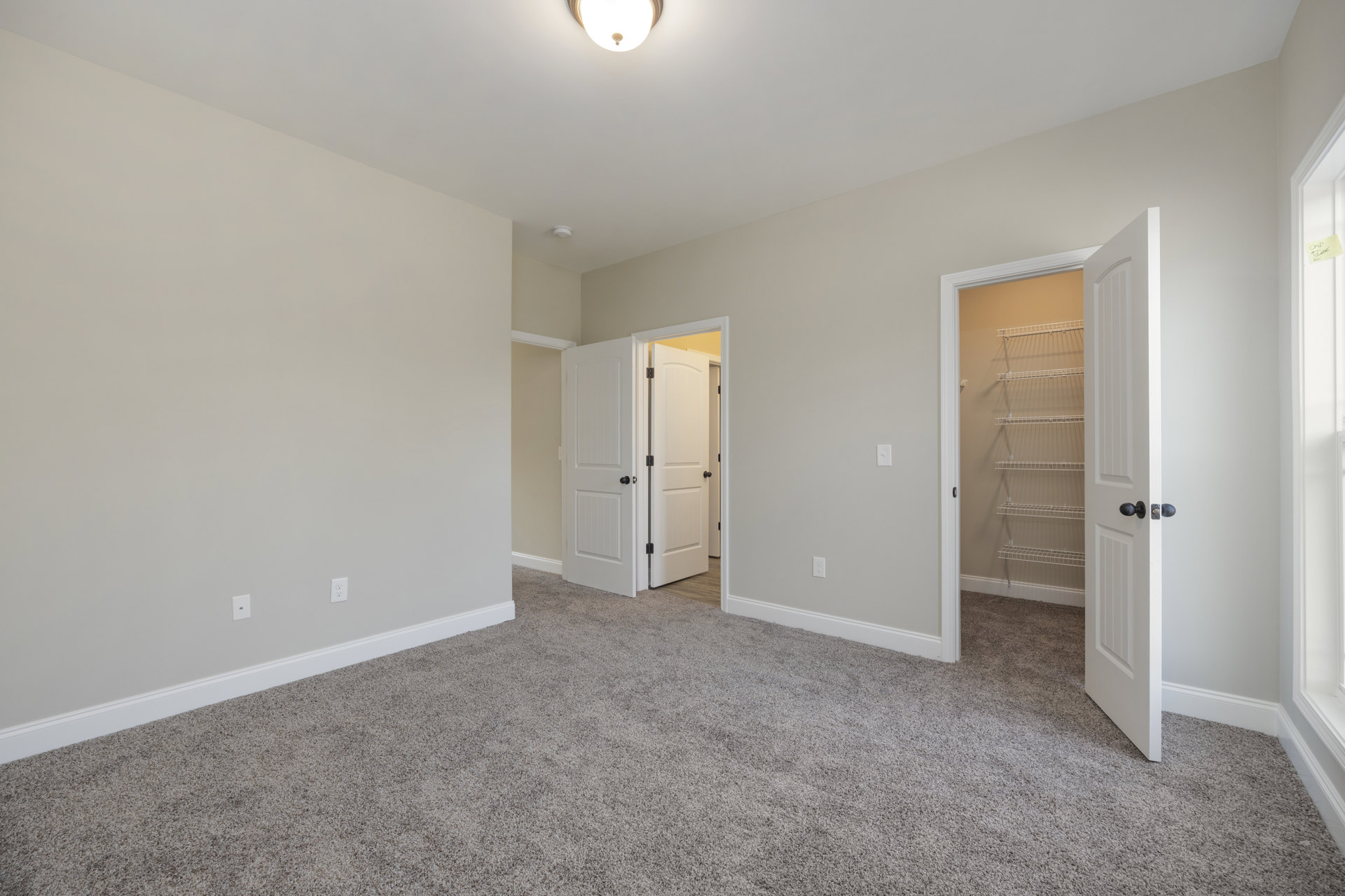 Carpeted room with white walls, open white door featuring black knob, built-in white closet shelves, and ceiling light fixture