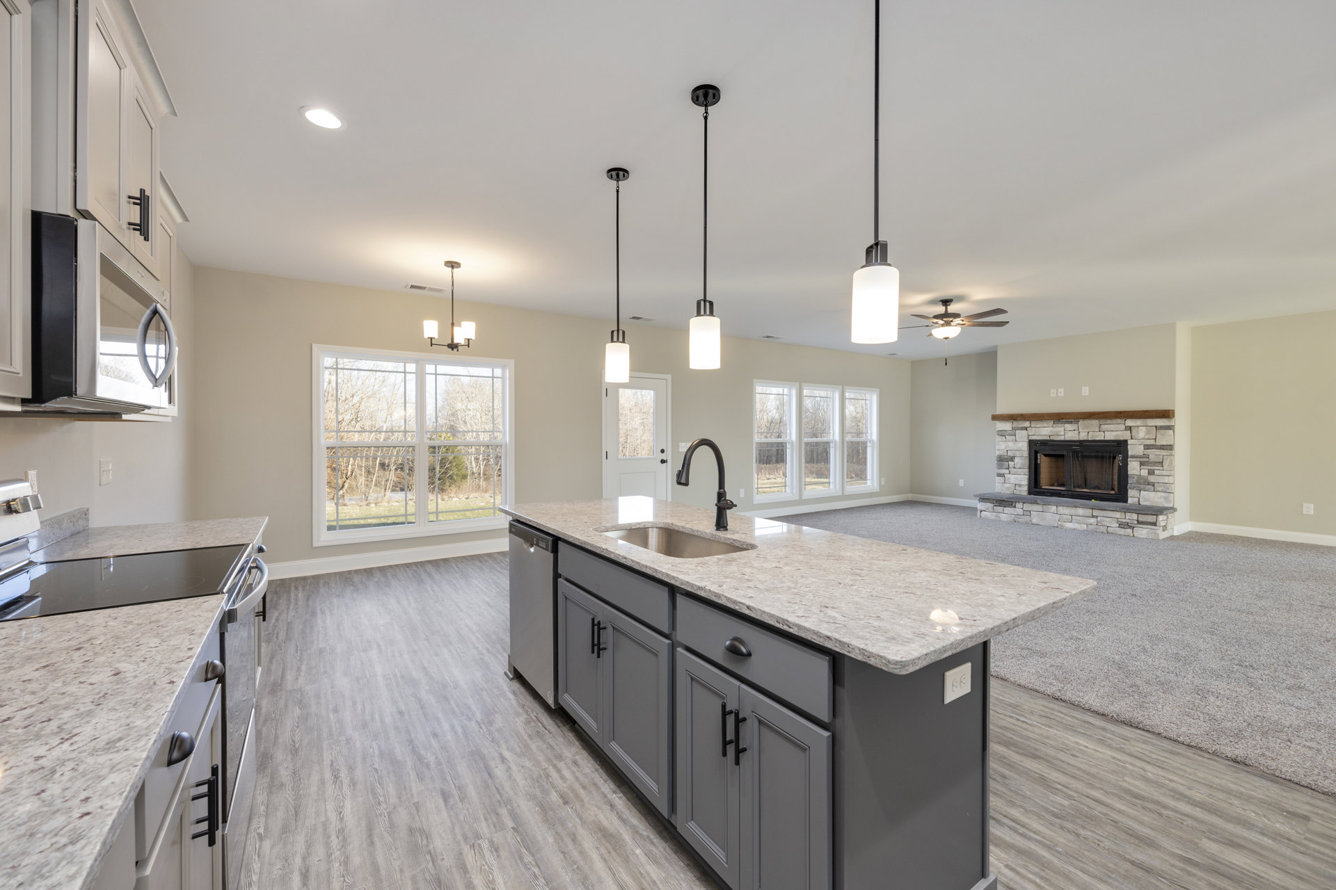 Open kitchen with white cabinetry, large central island featuring stone countertop and built-in sink, black-framed fireplace set into tiled wall, wide window overlooking trees
