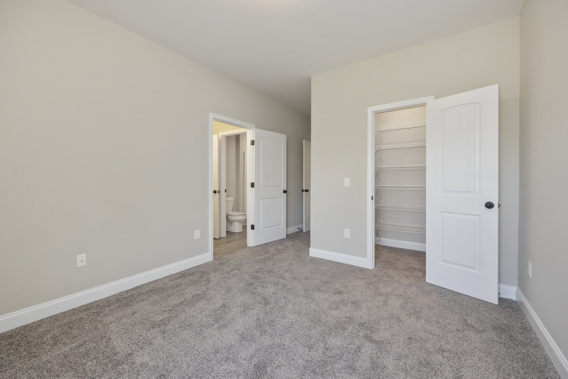 Carpeted room with white walls, two open white doors with black knobs, and a closet featuring a white shelf
