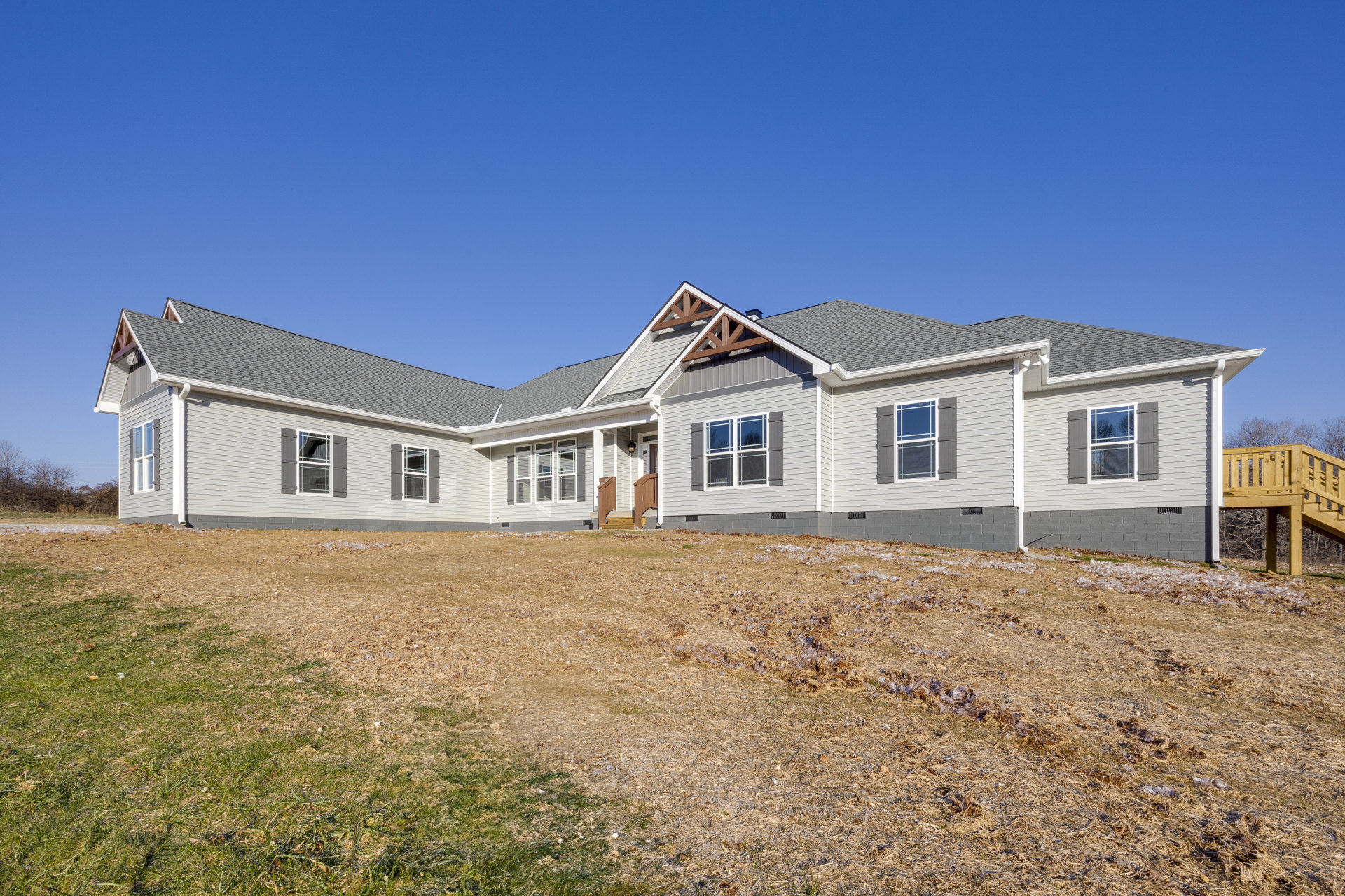 White two-story house with gabled roof, wide front porch, wooden stairs, and grassy hill in foreground under clear blue sky