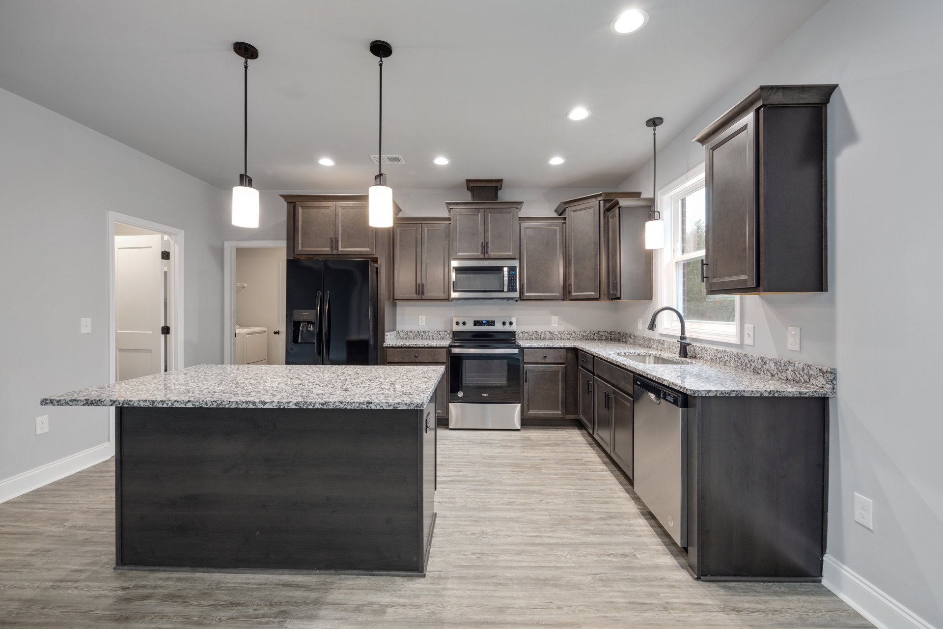 Granite countertops with black appliances, white cabinetry, tile backsplash, stainless steel microwave, and recessed ceiling lighting in a modern kitchen.