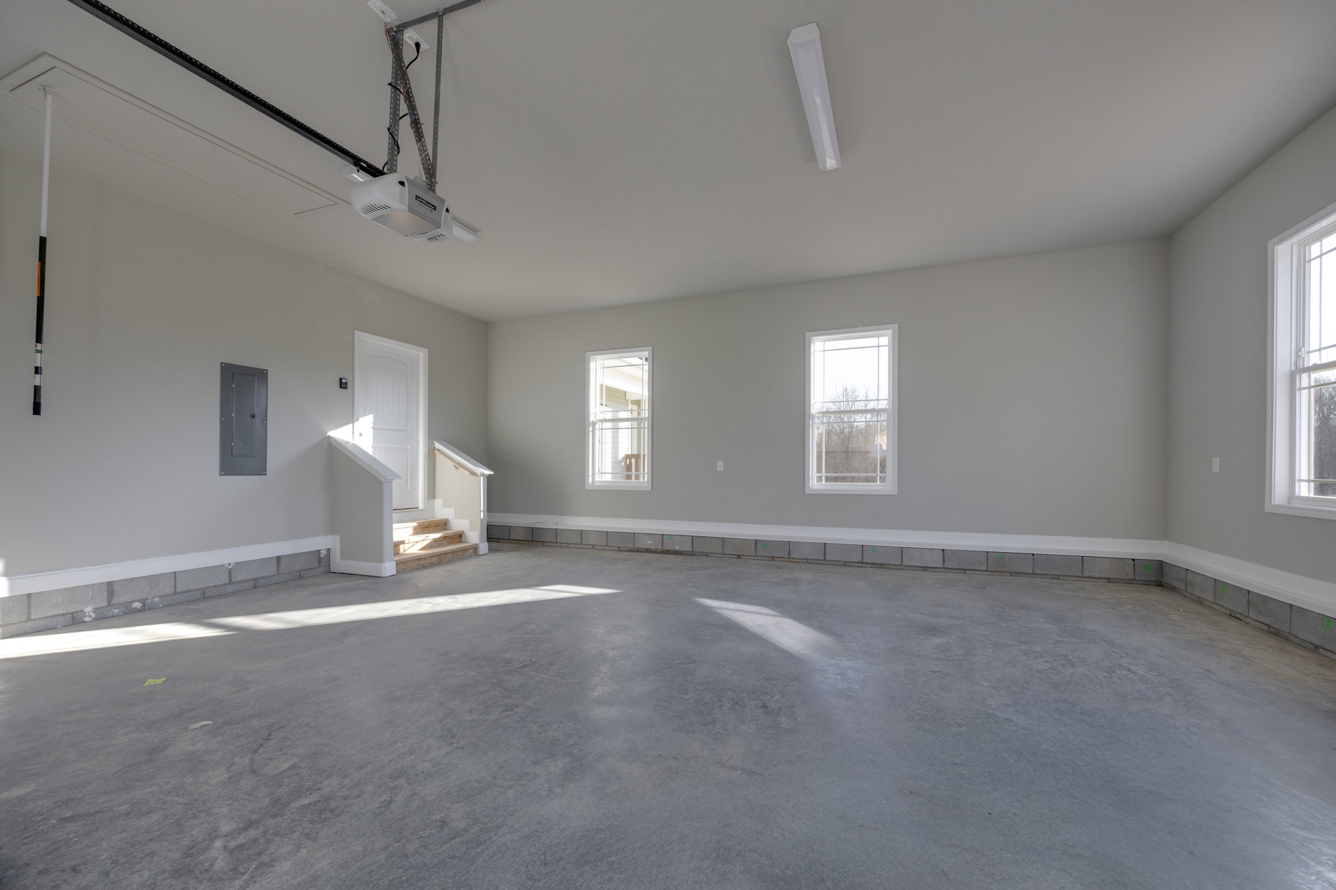 Concrete floor room with white-framed windows, grey door with square lock, and modern staircase; trees visible outside.