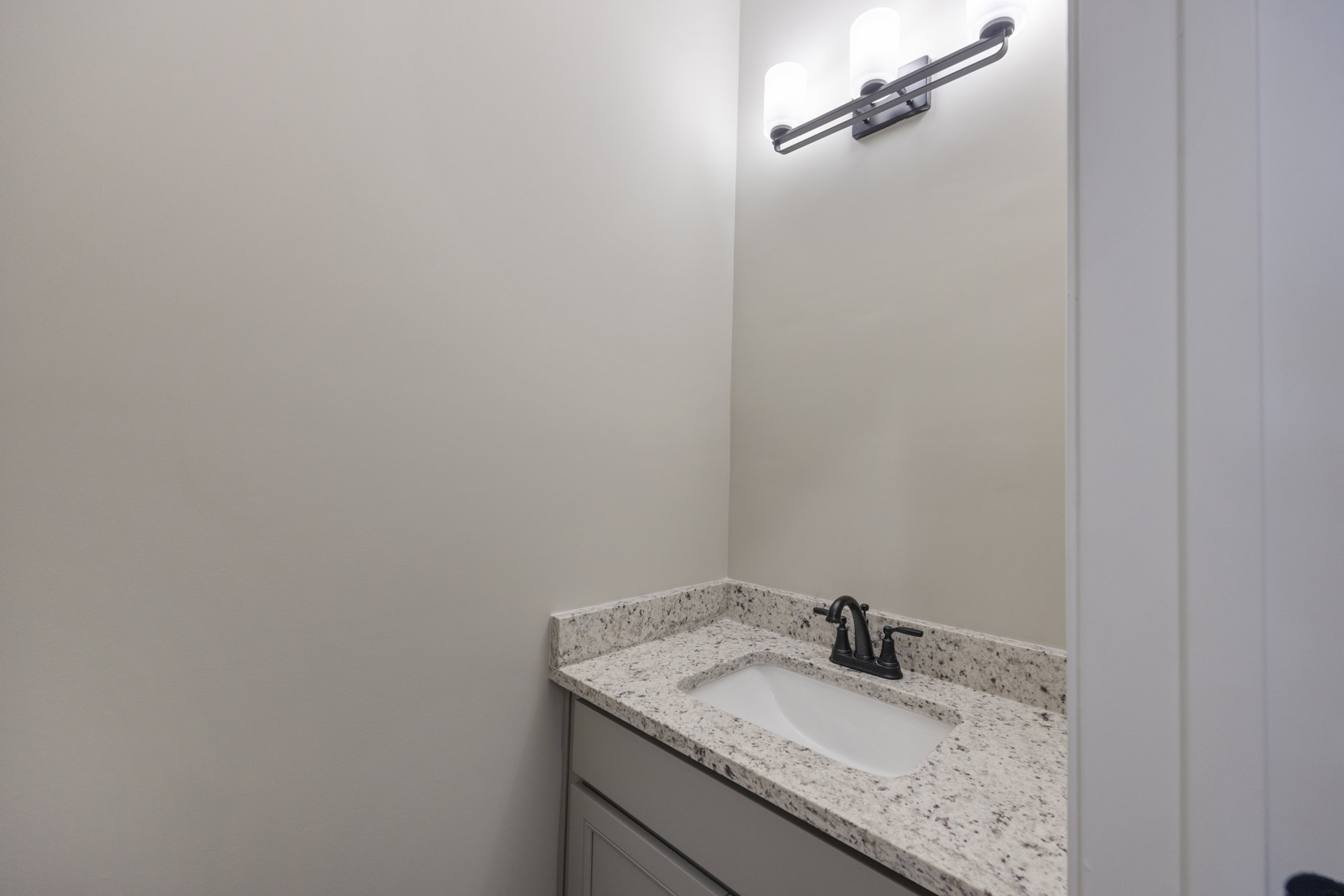 Marble countertop with rectangular white sink, matte black faucet, wall-mounted light fixture, and neutral tile backsplash