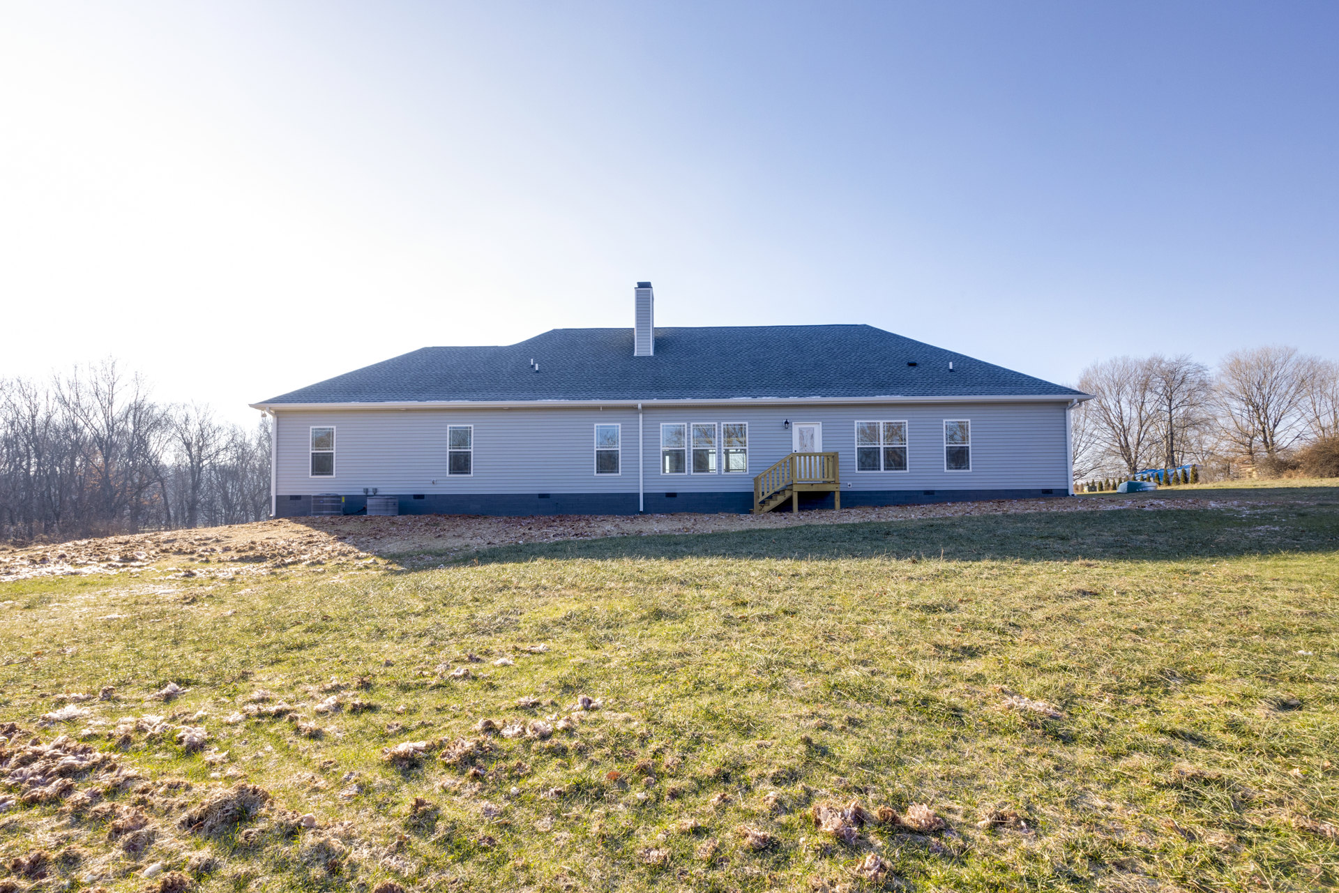 Two-story farmhouse with white siding, covered front porch with wooden railing, brick chimney, large windows, green lawn, and mature trees in the yard.