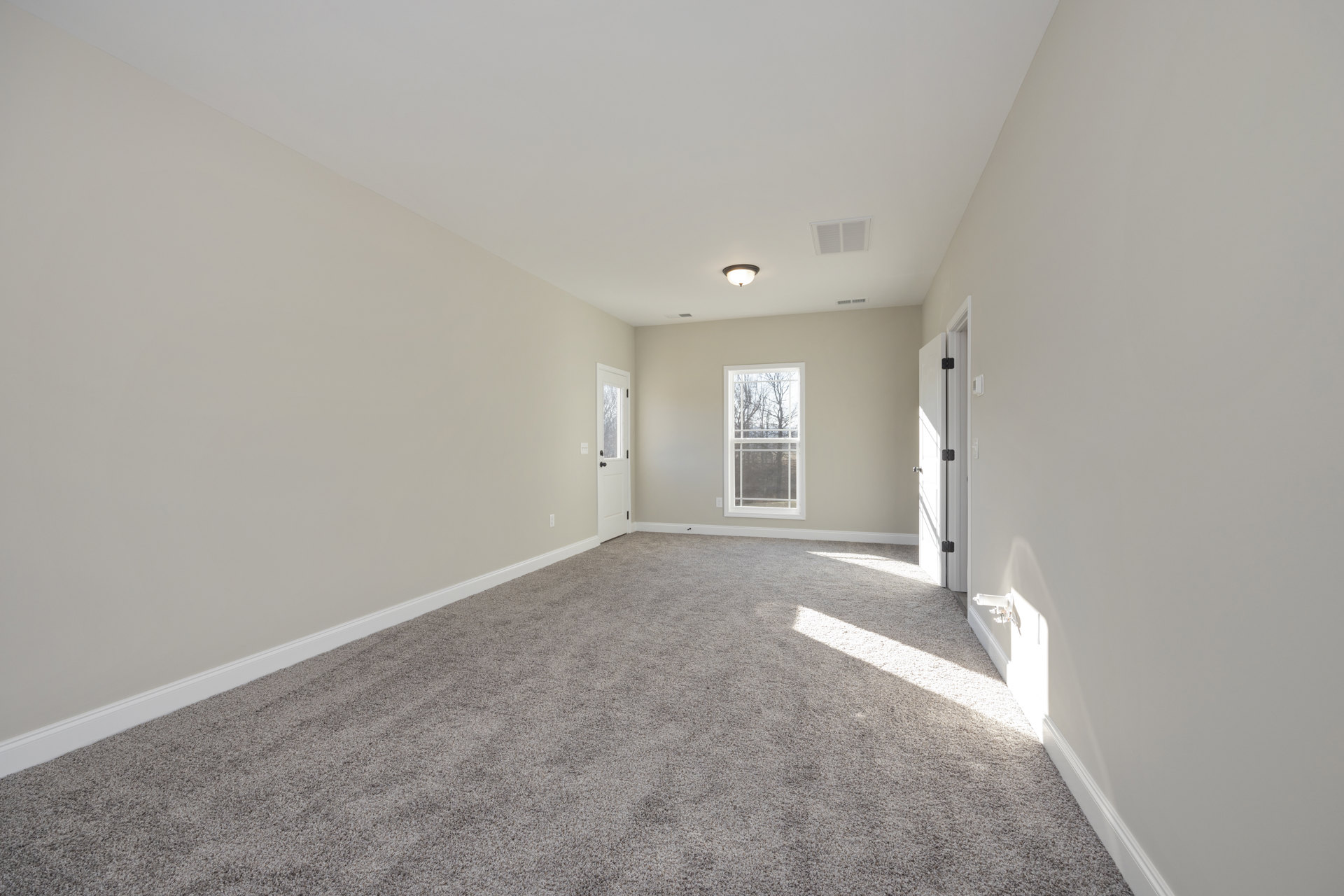 Carpeted bedroom with white walls, ceiling vent, large window overlooking trees, and a closed door