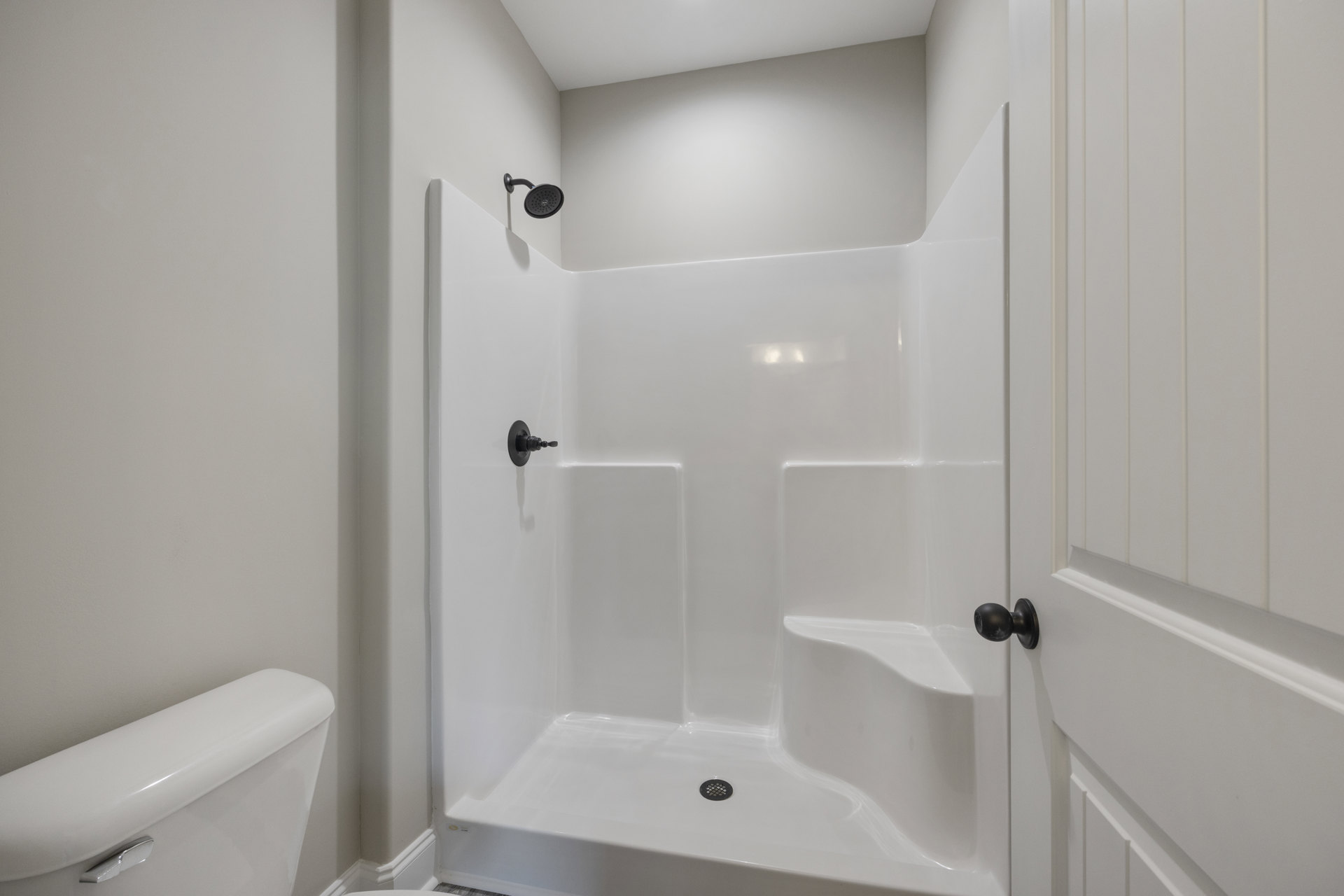 Glass-enclosed shower with matte black hardware, white subway tile walls, and a modern rainfall showerhead in a bright bathroom.