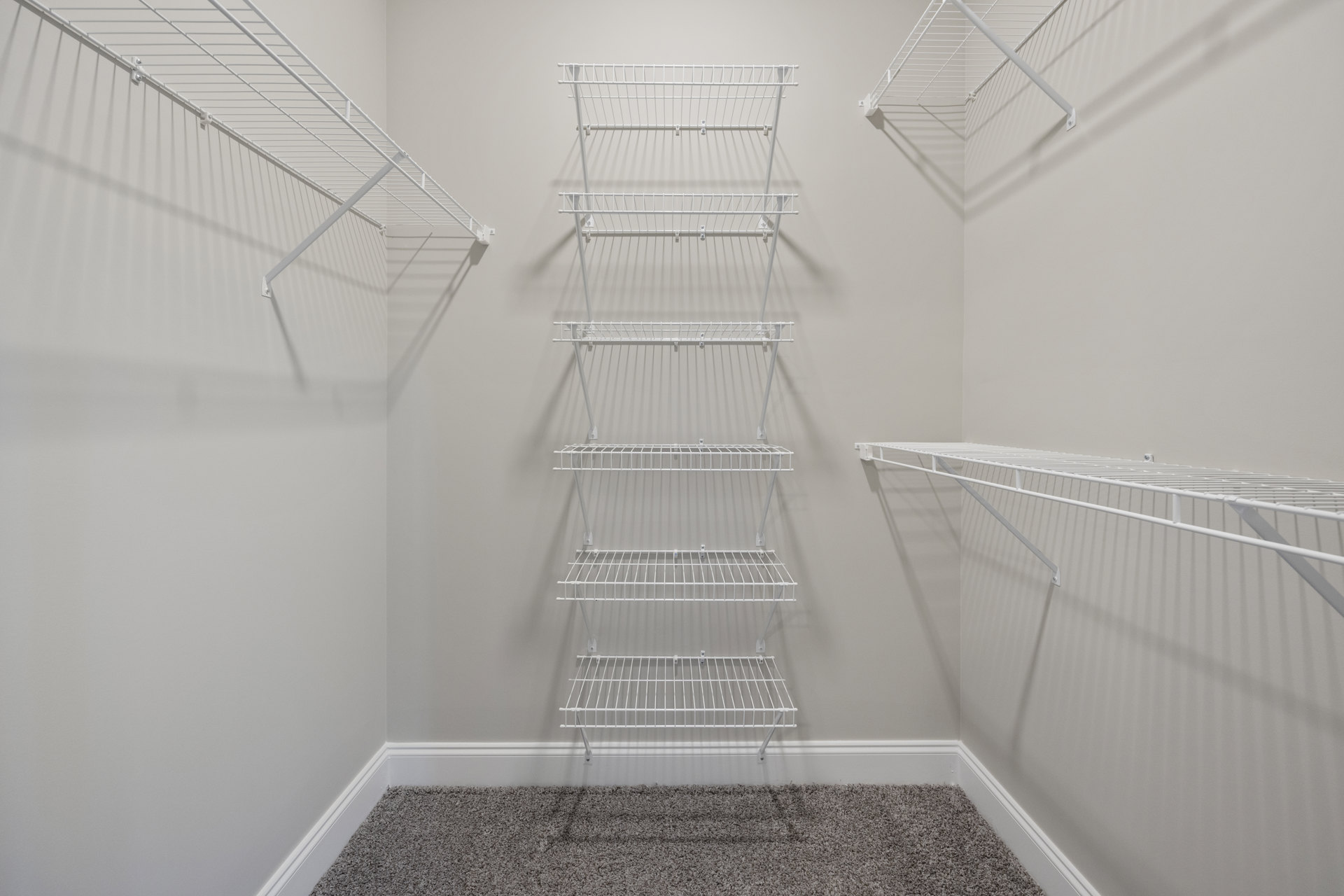 White wire shelving mounted on a wall above beige carpet flooring in a small indoor room.