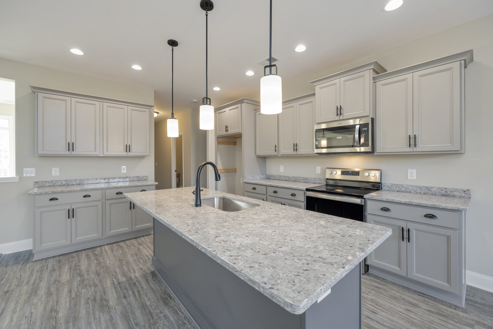 Spacious kitchen featuring a large granite island, tile backsplash, white cabinetry, stainless steel appliances including a microwave with illuminated interior, stove with digital