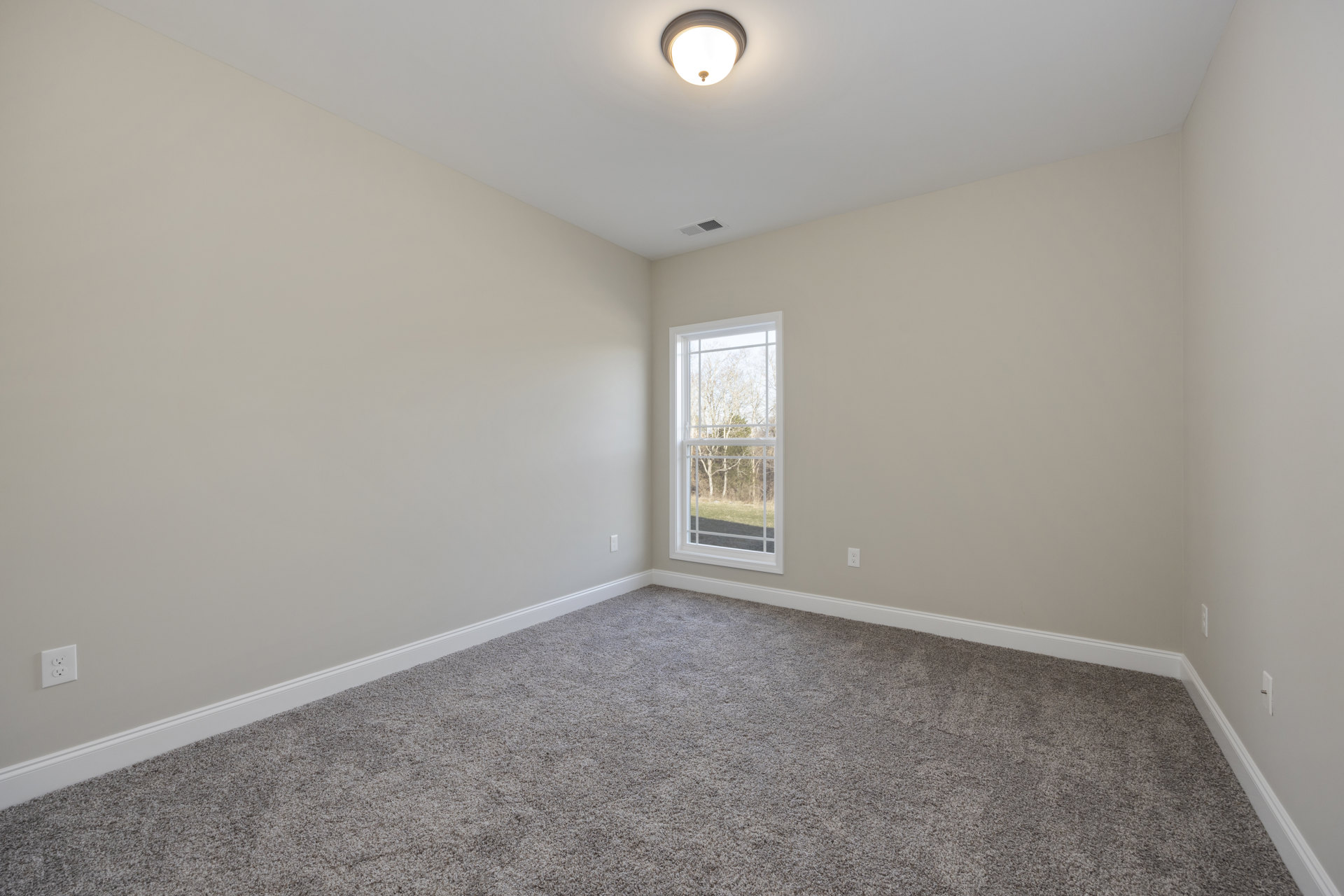Bedroom with beige carpet, white walls, large window overlooking trees, recessed ceiling light, and white electrical outlet