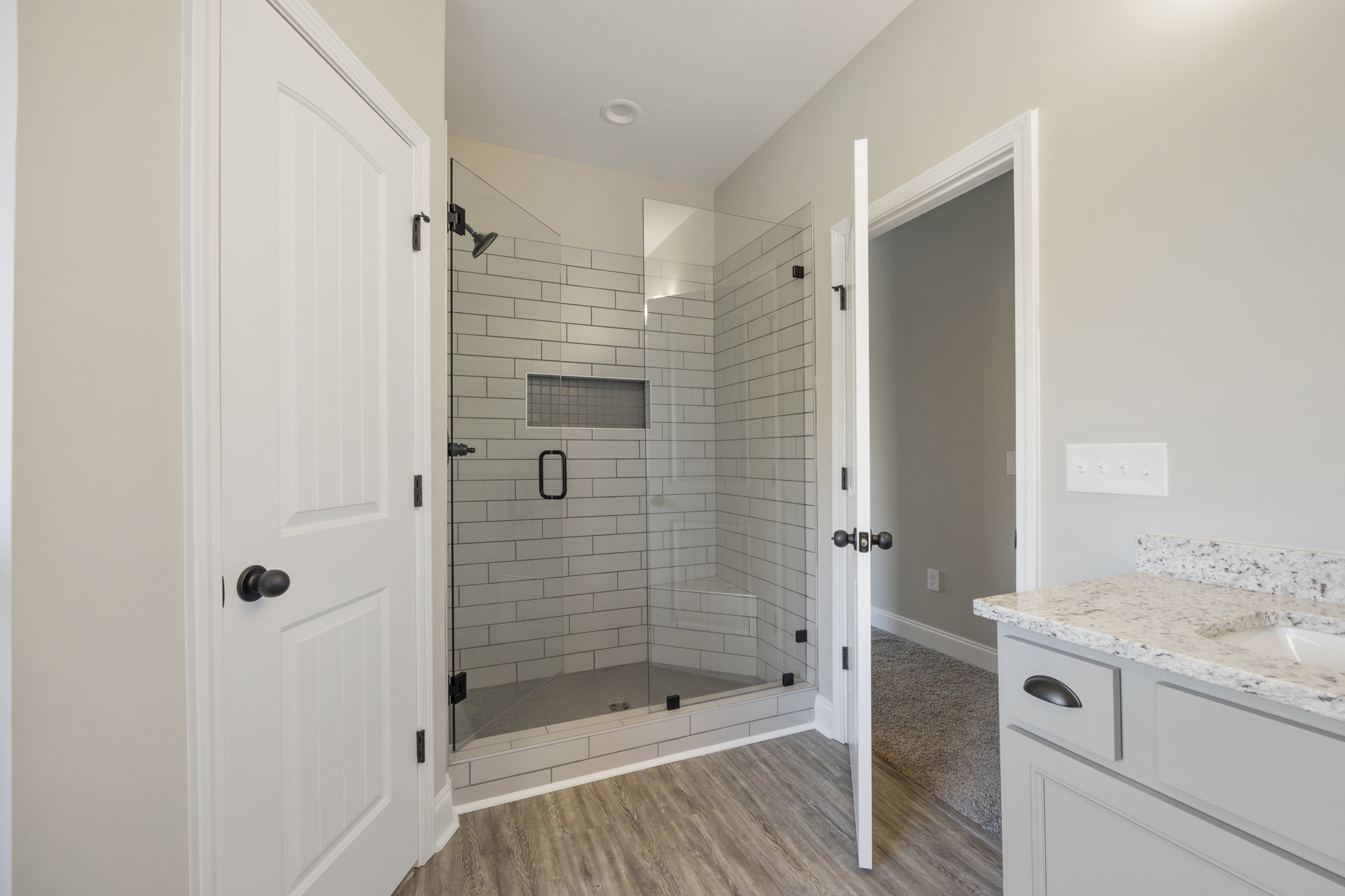 Bathroom featuring a glass shower with white tile walls, white countertop with drawers, row of light switches, and black door knob on a white cabinet.