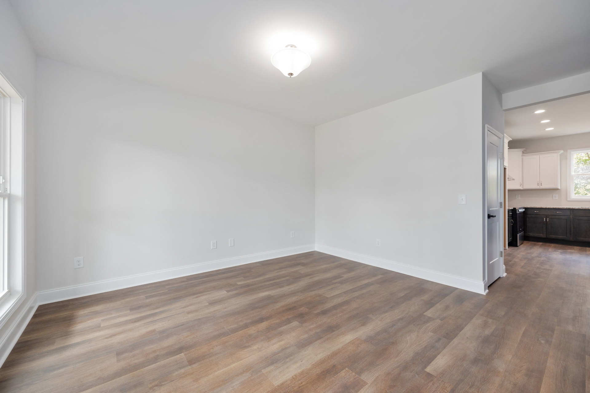 Open-concept room with hardwood flooring, modern pendant light fixture, white walls, and a window with a white frame