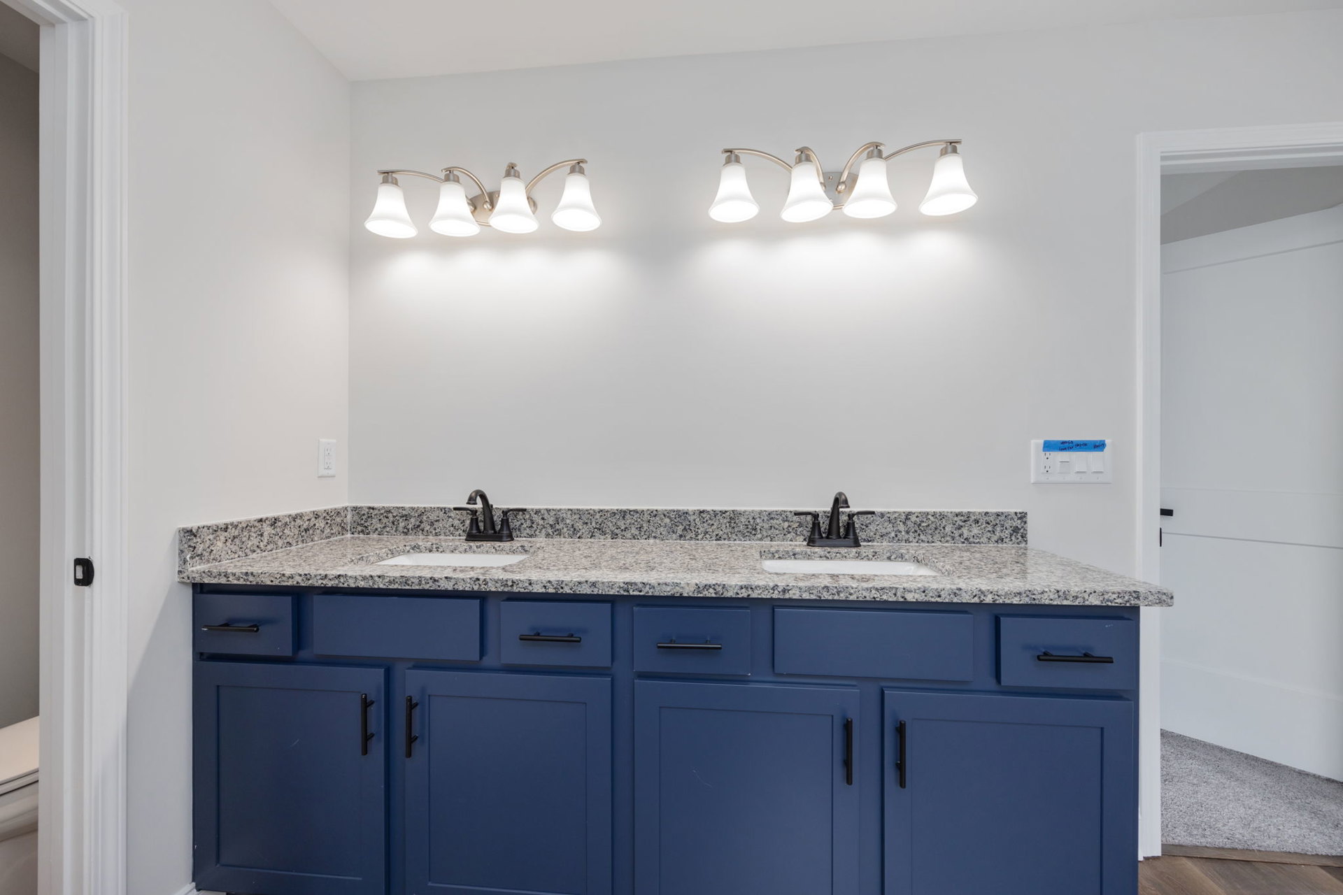 Blue bathroom vanity with black handles, marble countertop, white tile backsplash, double light fixture above mirror, recessed ceiling lights, chrome faucet, and drawers.