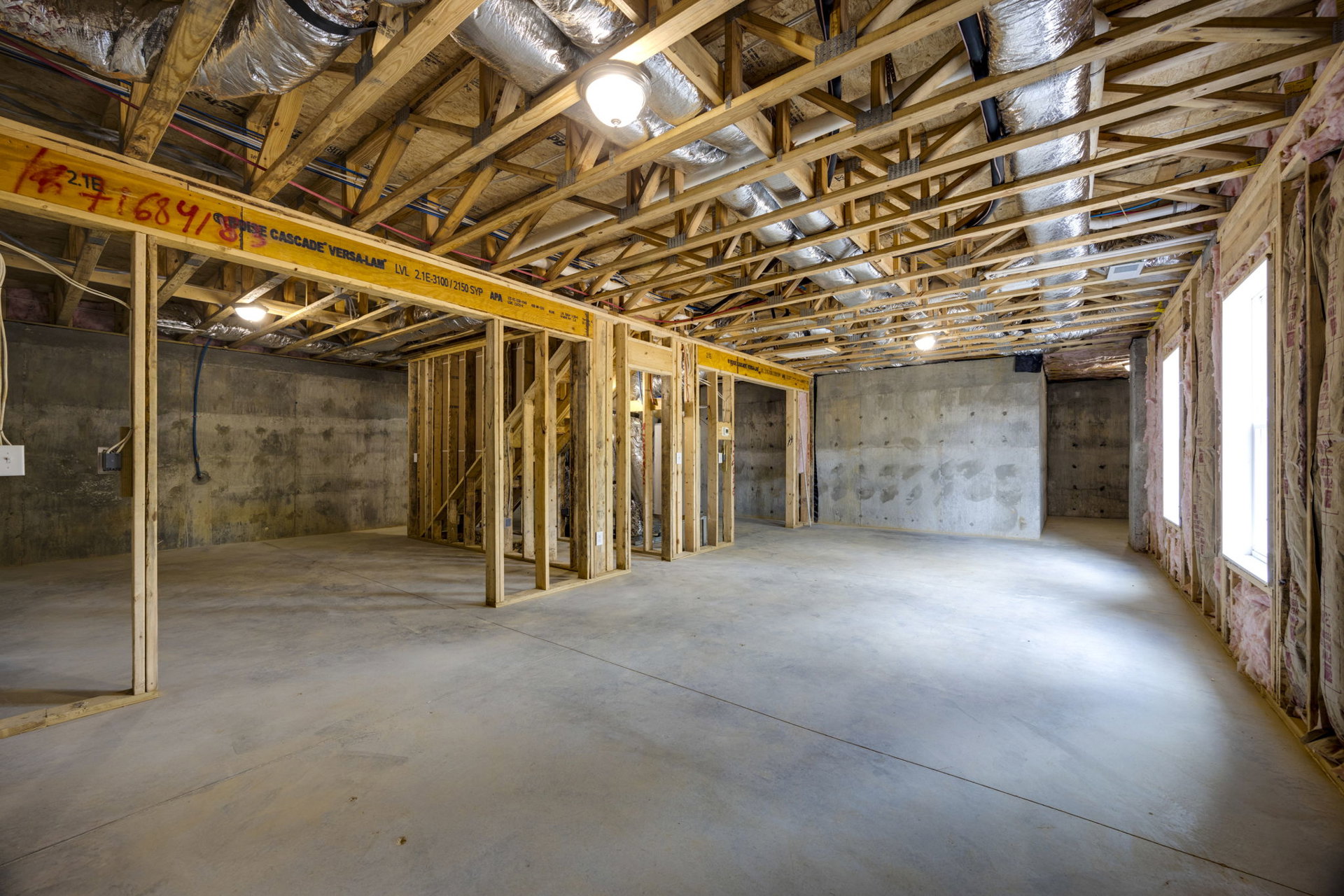 Exposed wood ceiling beams, concrete walls with visible holes, concrete floor, single ceiling light fixture