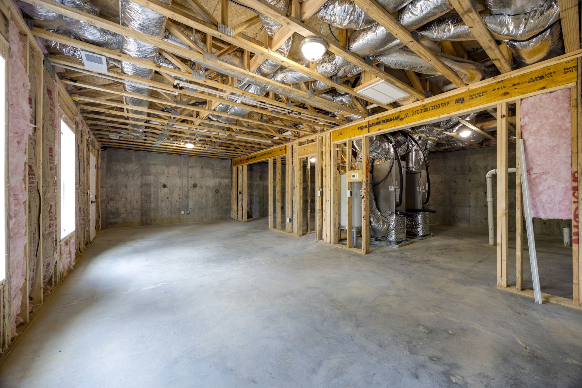 Yellow structural beam and exposed silver metal ceiling with visible air ducts, wood framing, and a water tank in an unfinished basement room.