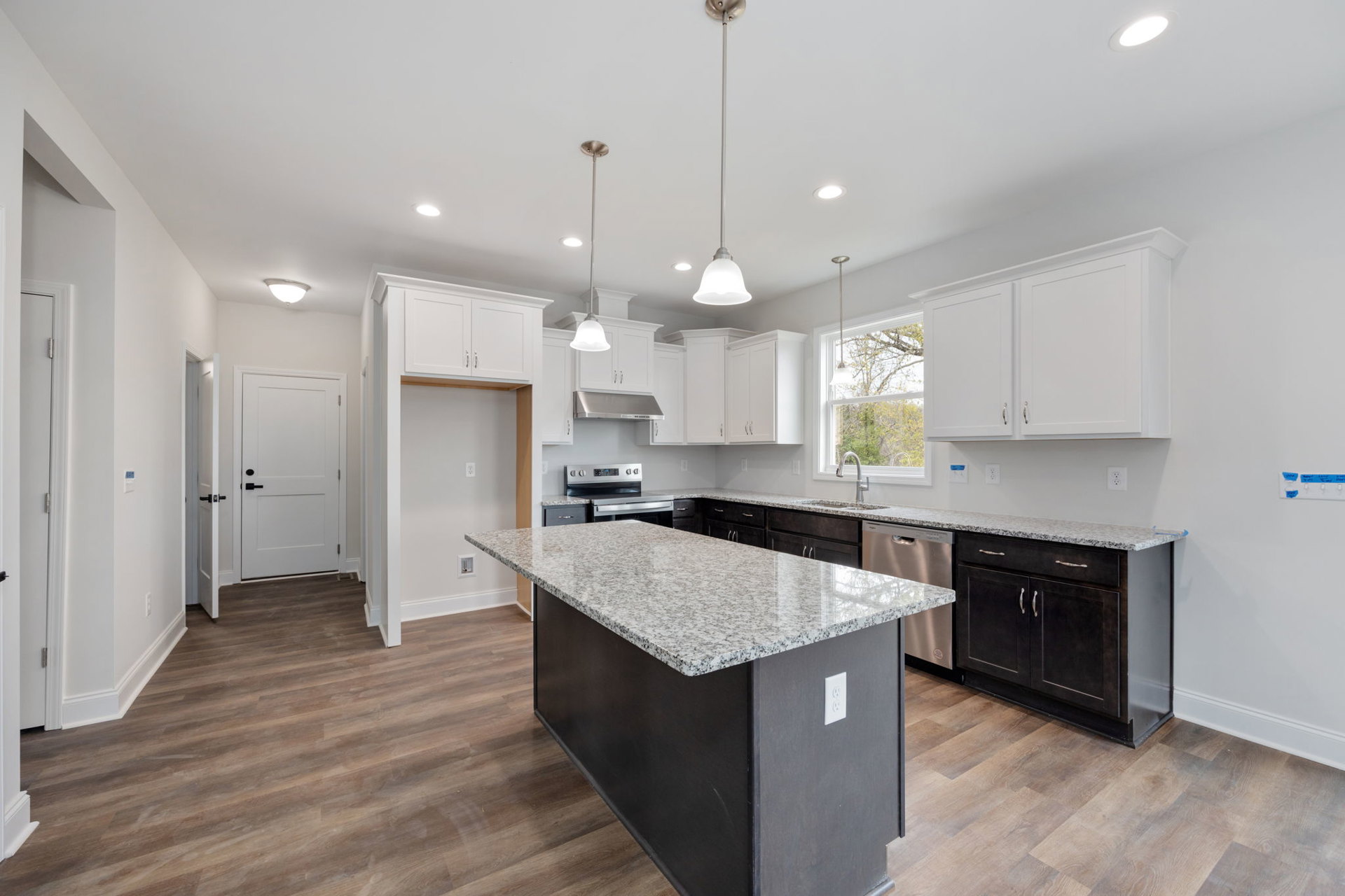 Granite kitchen island with black cabinetry, stainless steel stove, marble countertops, white door with black handle, ceiling light fixture, tile flooring, and undermount sink.