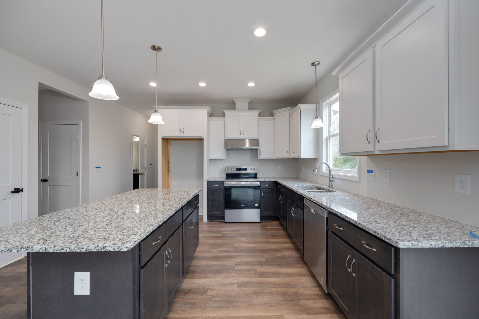 Granite countertops and white cabinets in a kitchen, stainless steel oven, white electrical outlet, recessed ceiling lights, white door with black handle