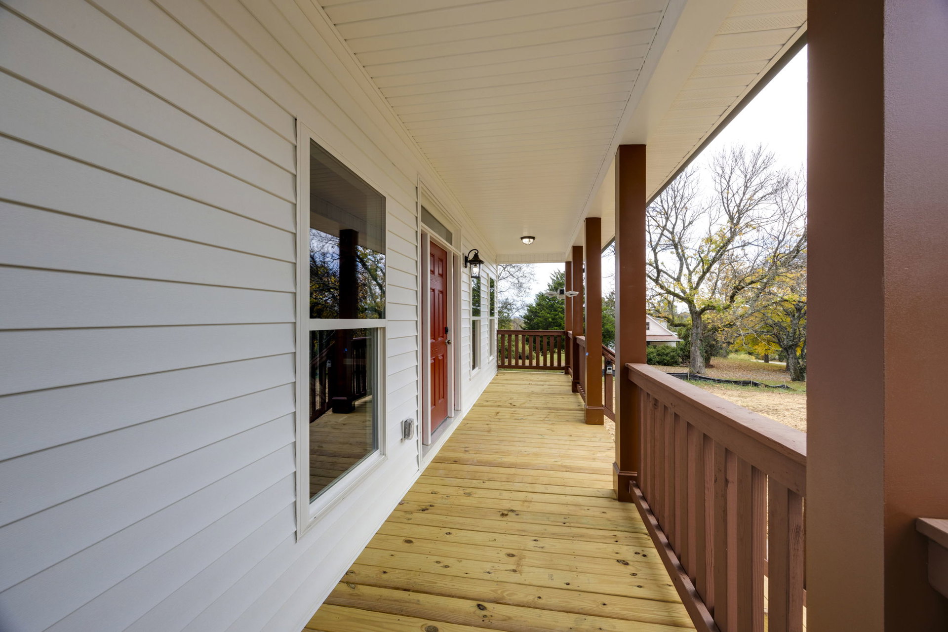 White siding house with red front door, wooden deck and brown railing, leafless tree in background