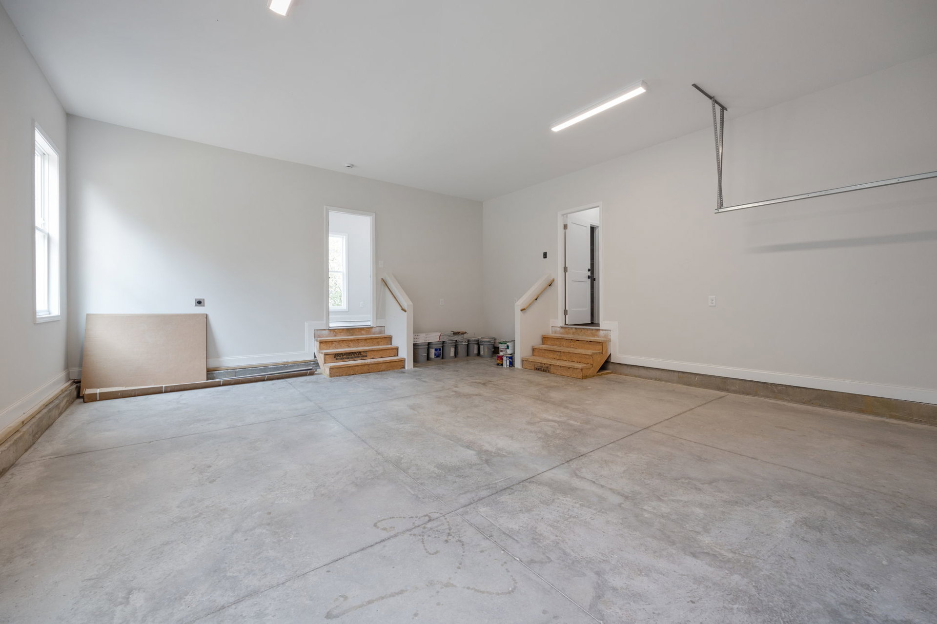 Concrete floor with wooden steps leading to a white door featuring a window and black handles, plaster walls, and ceiling in a modern interior room.