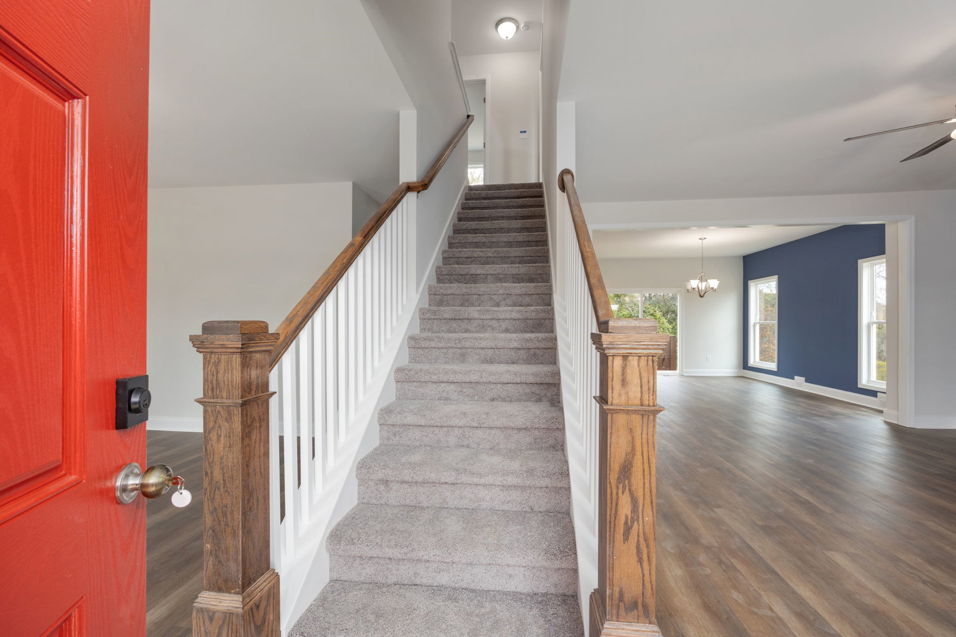 Carpeted staircase with wooden handrail, hardwood floor, blue accent wall, and white interior door with silver knob