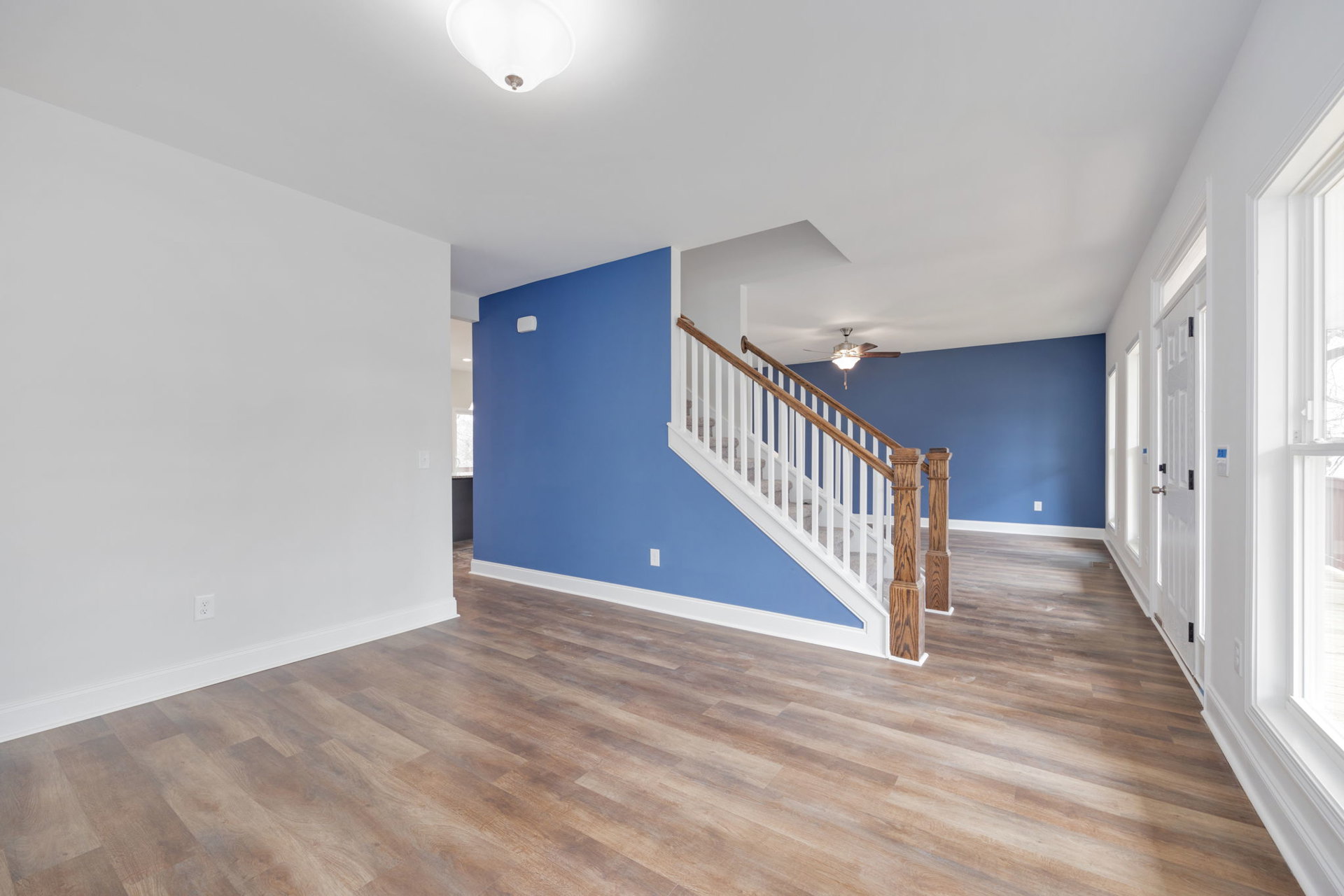 Blue and white room featuring hardwood floors, a staircase with wooden handrail, ceiling fan with light fixture, and plaster walls.