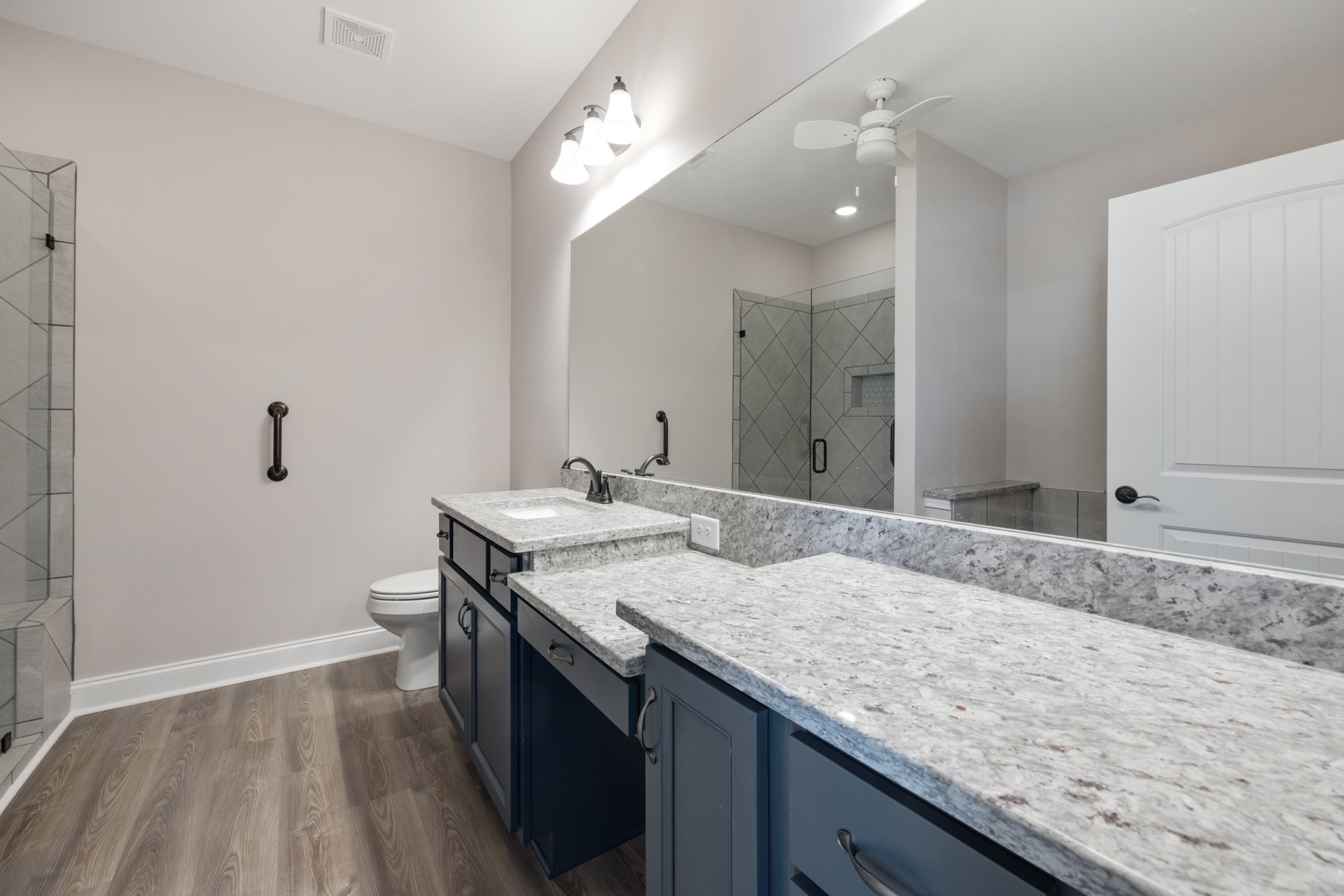 Bathroom with marble countertops, large wall mirror, white cabinetry, tile backsplash, three-light fixture above mirror, closed toilet, white door and door frame