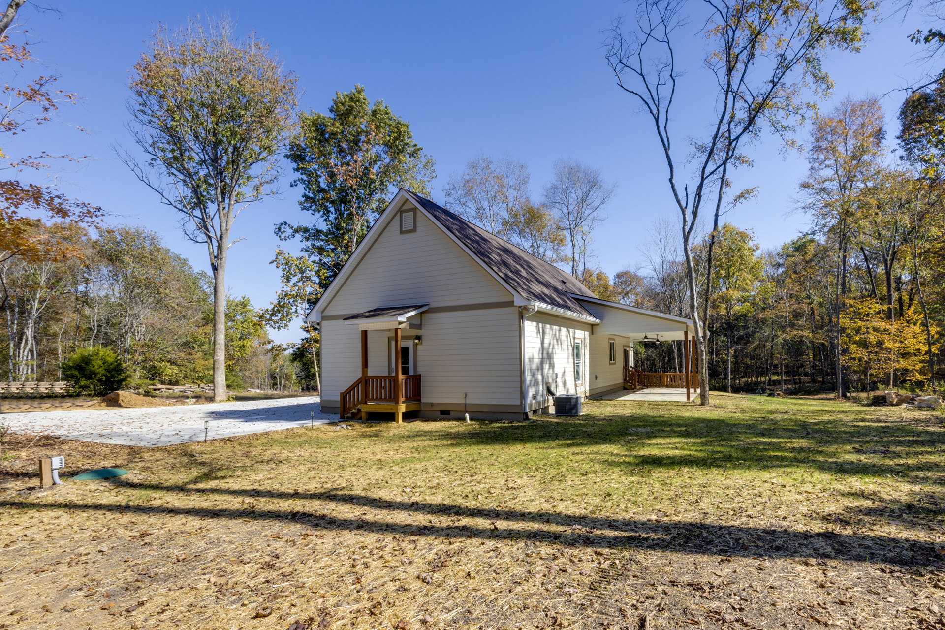 Two-story farmhouse with white siding, wooden porch and railing, surrounded by green grass and mature trees with leafy canopies