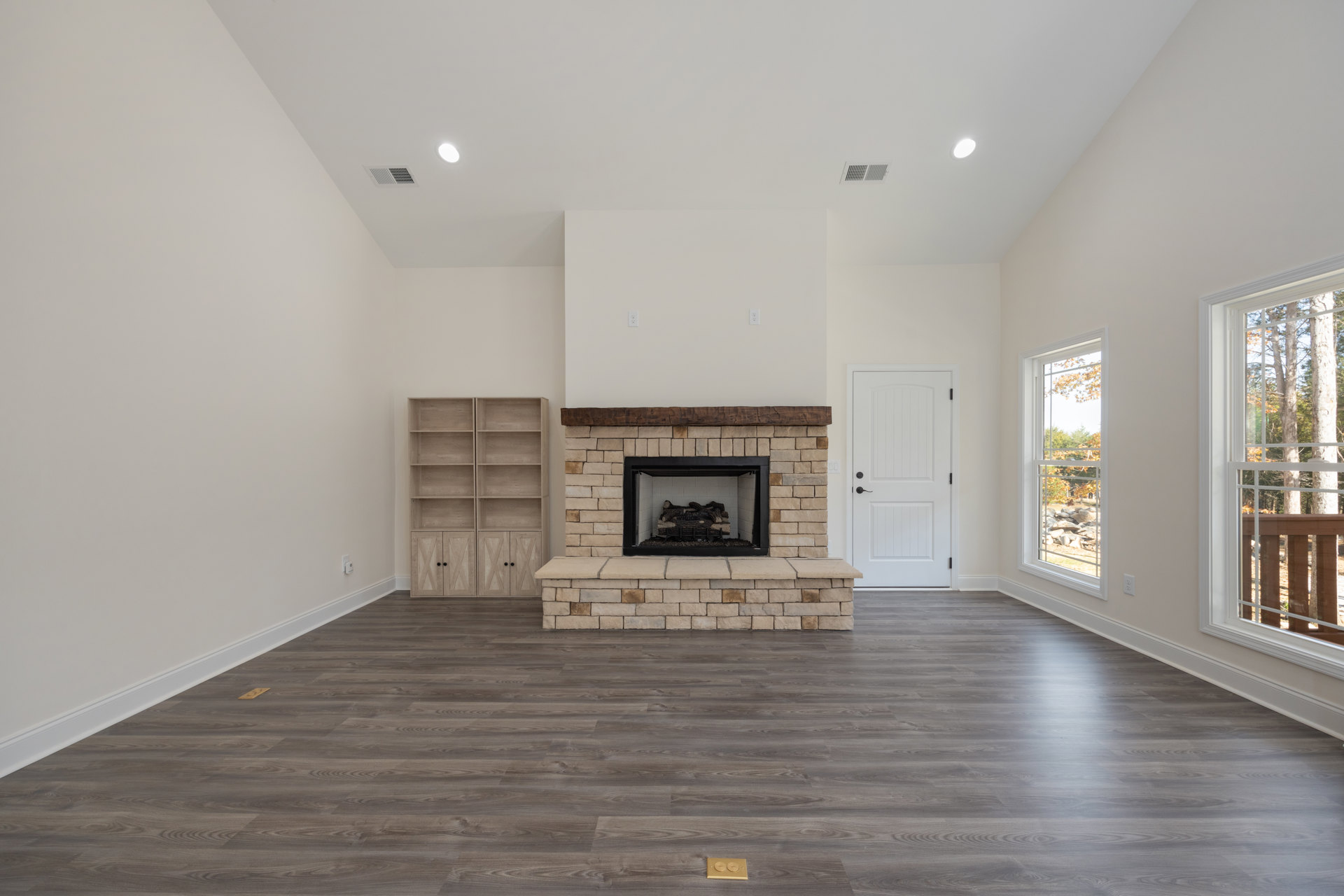 Living room with light wood flooring, white plaster fireplace stacked with logs, built-in wooden shelves with black handles, and white door with black hardware.