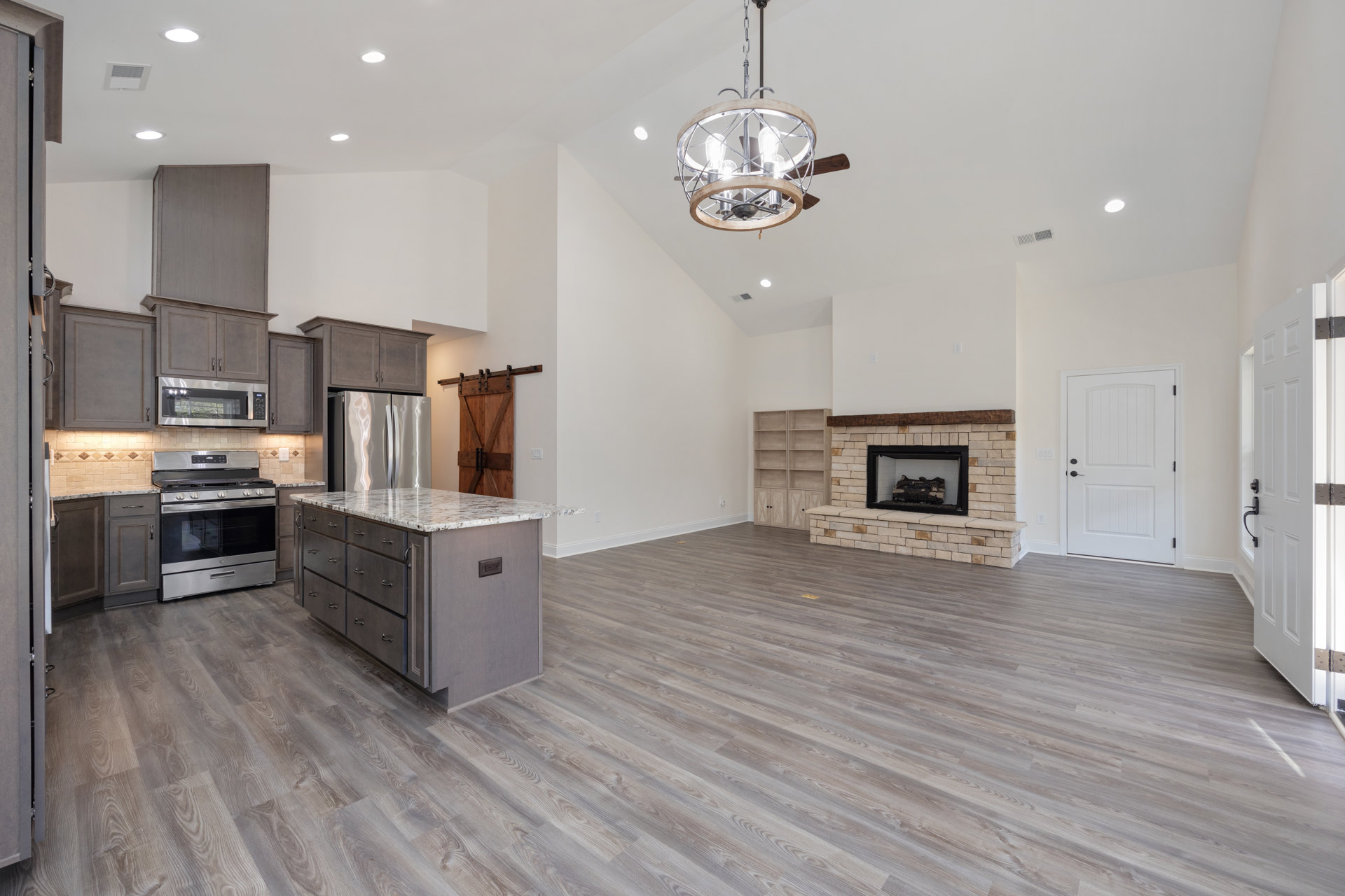 Spacious open floor plan featuring a kitchen with a central island, stainless steel refrigerator, stove and oven, white cabinetry with black handles, wood flooring, ceiling fan