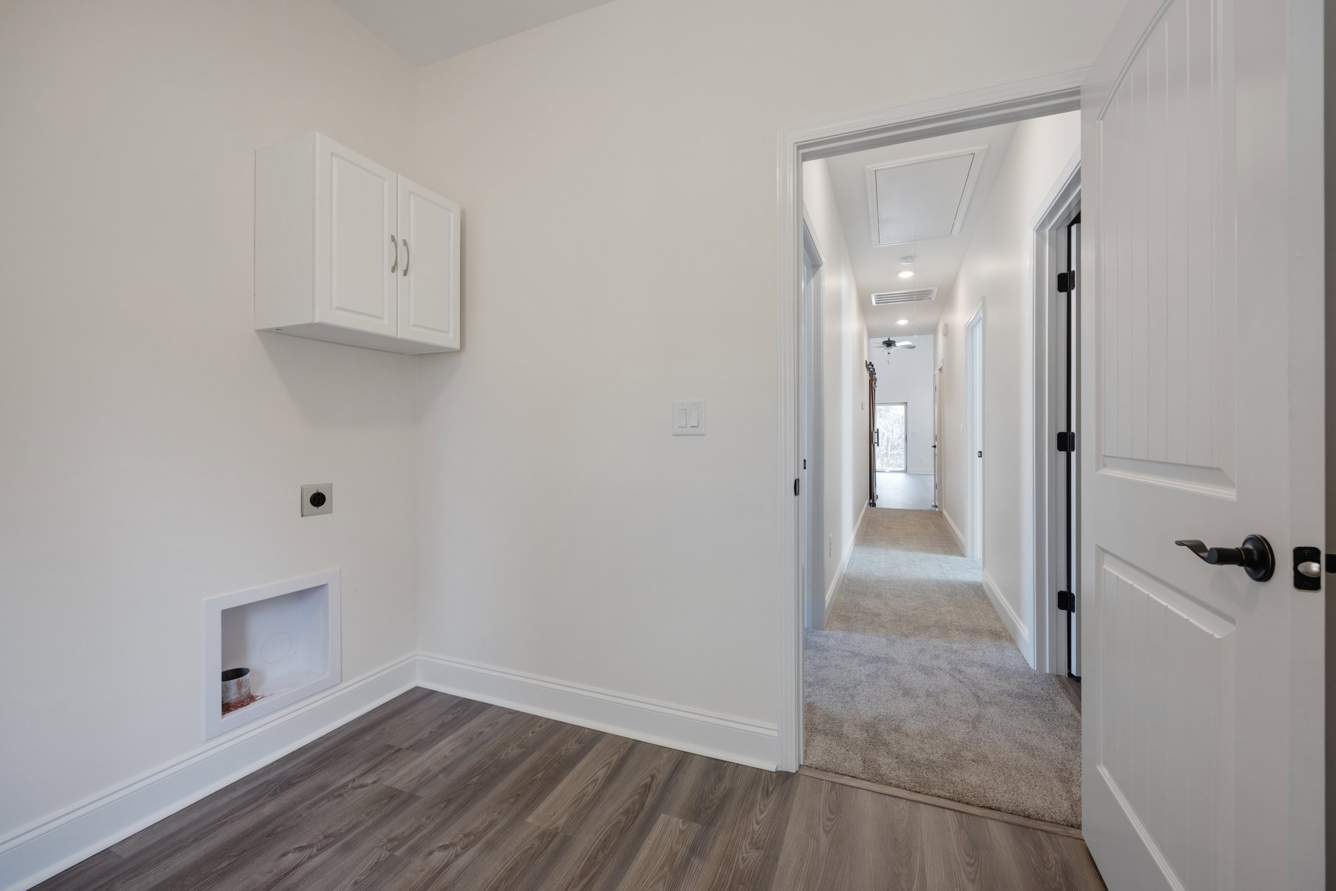 Hallway with light wood flooring, white walls, white baseboards, and a white ceiling featuring a square window; white cabinet with silver handles visible, paint bucket placed